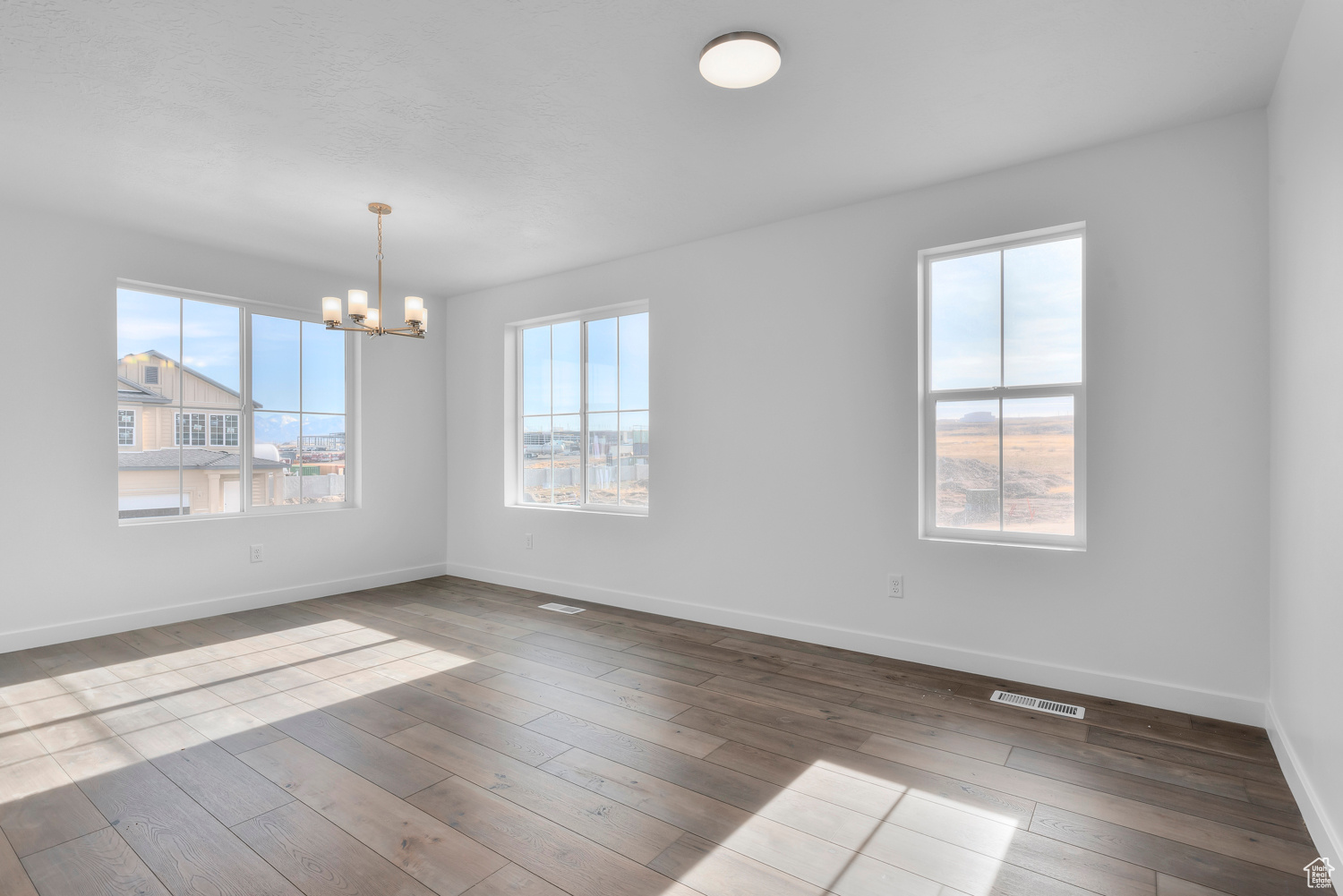 Spare room with hardwood / wood-style floors and an inviting chandelier