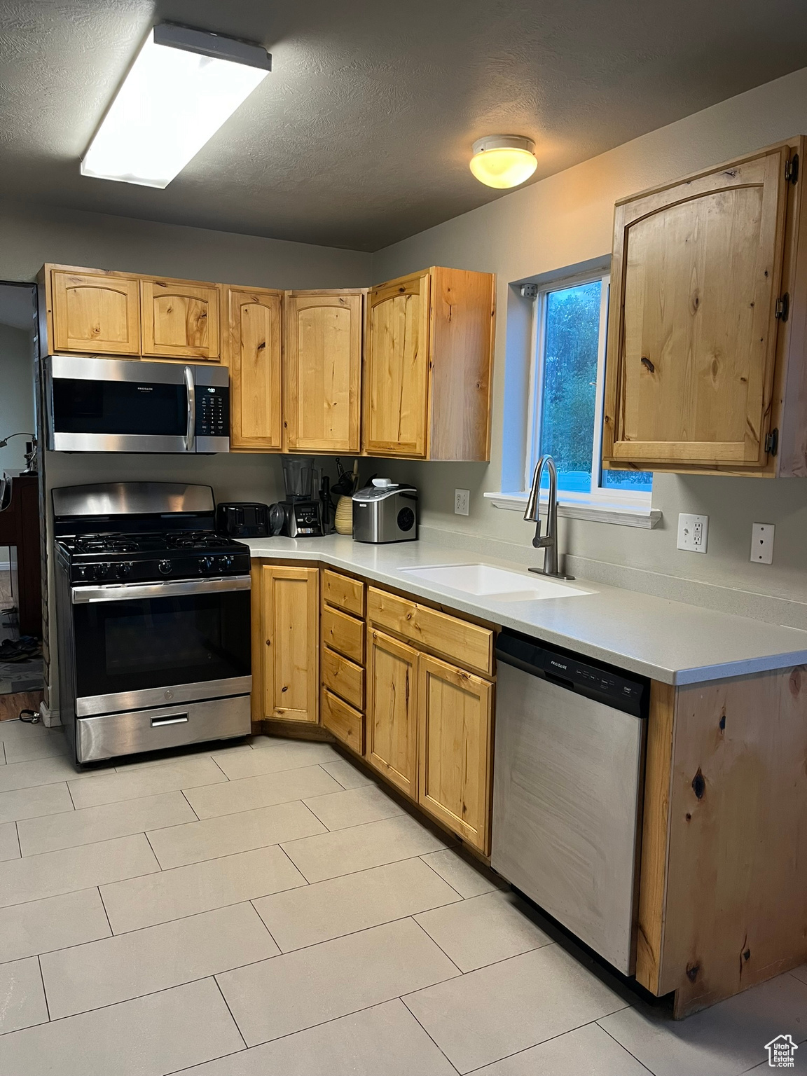 Kitchen with a textured ceiling, sink, light tile patterned floors, and appliances with stainless steel finishes