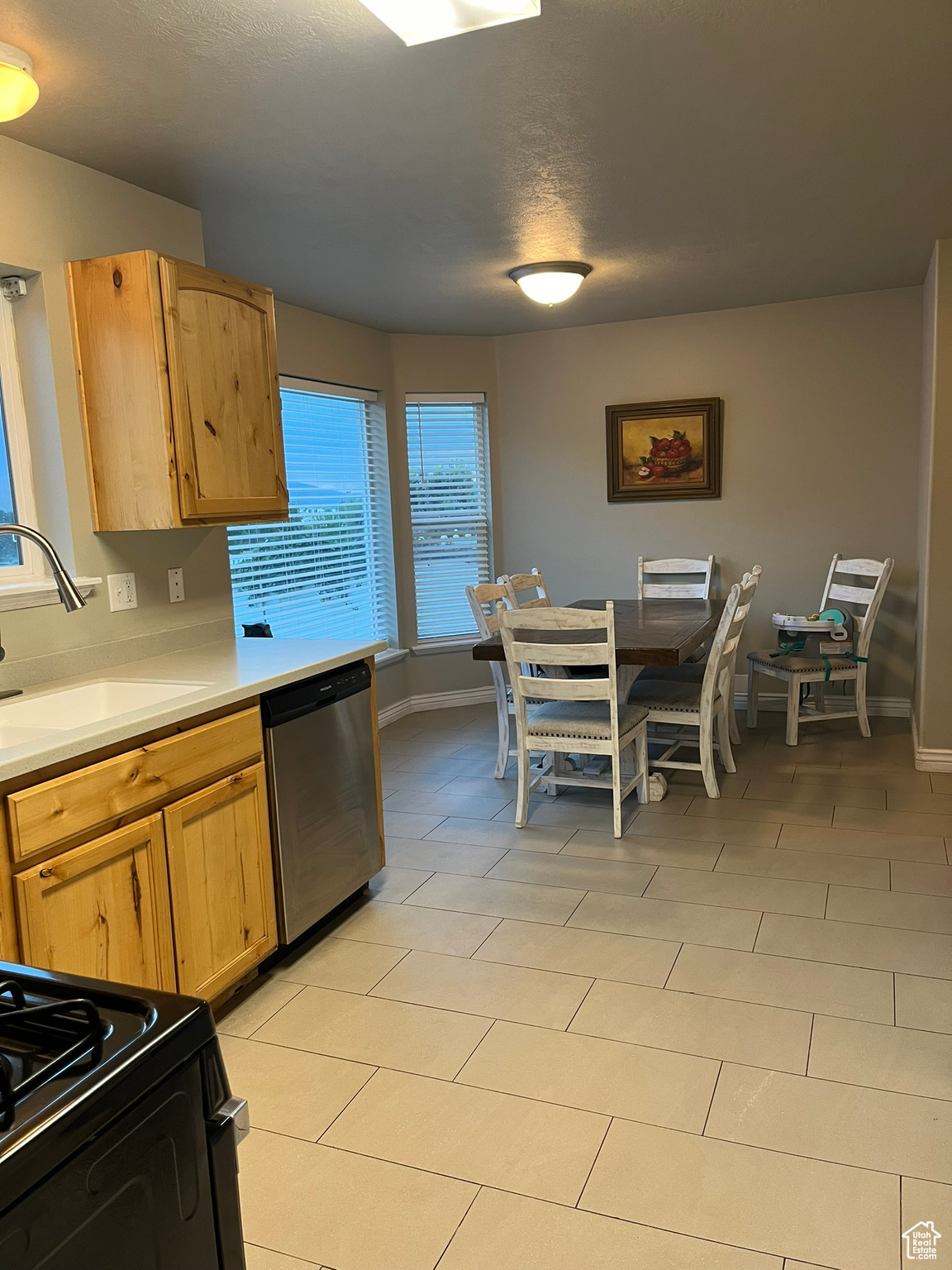 Kitchen with a textured ceiling, light tile patterned floors, stainless steel dishwasher, black range oven, and sink