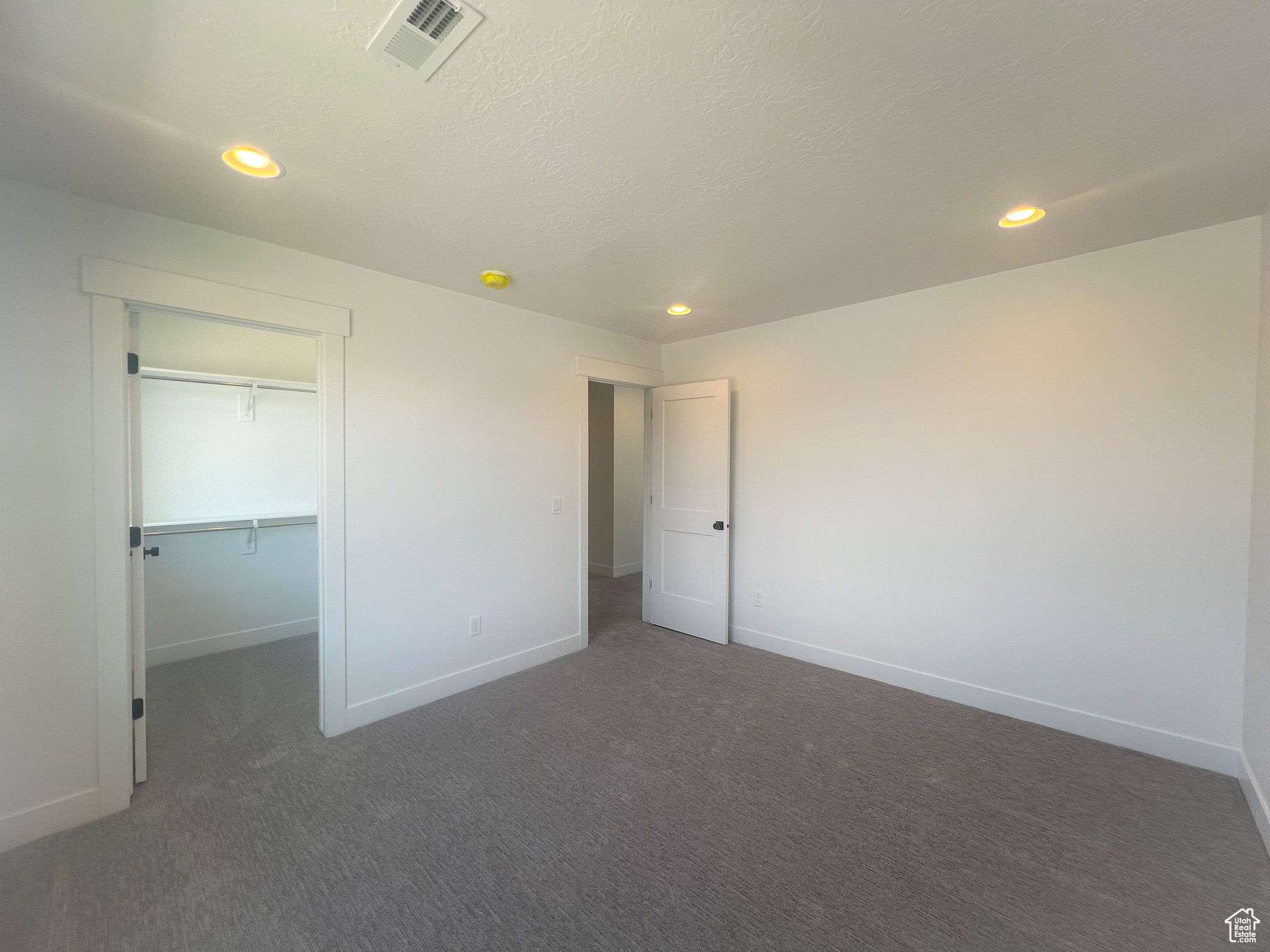 Unfurnished bedroom with a textured ceiling, dark carpet, a walk in closet, and a closet