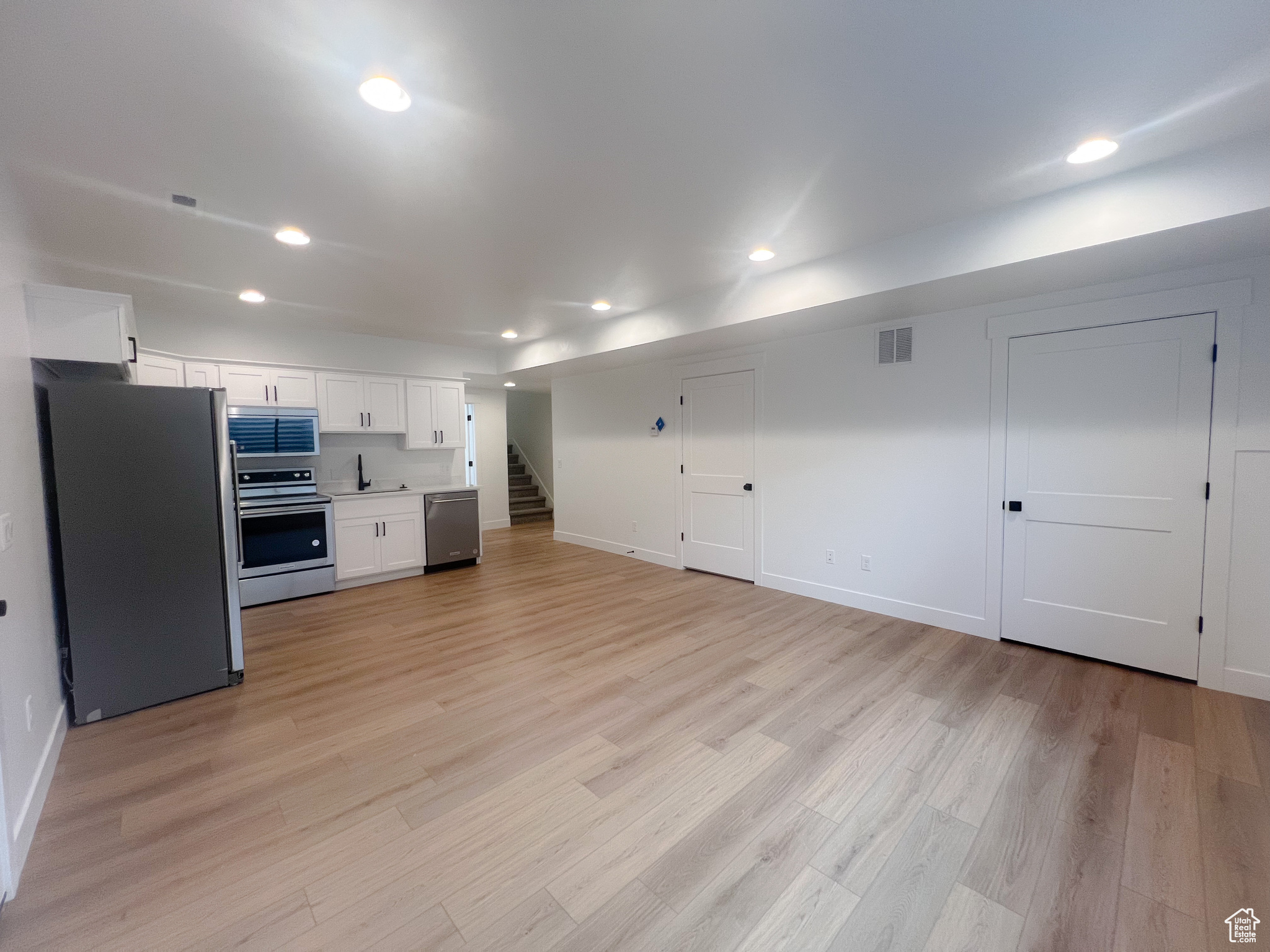 Kitchen with light wood-type flooring, appliances with stainless steel finishes, sink, and white cabinets