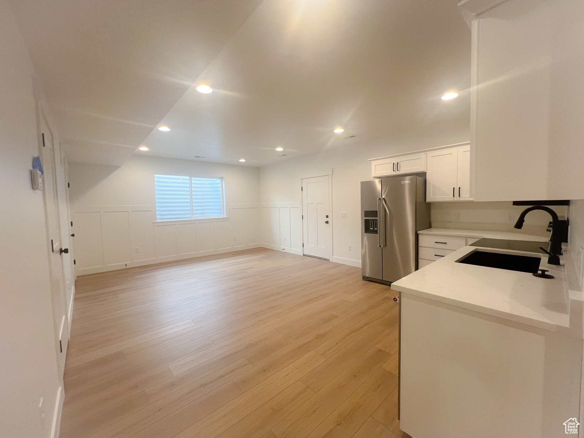 Kitchen featuring stainless steel fridge, light hardwood / wood-style floors, sink, white cabinetry, and light stone counters