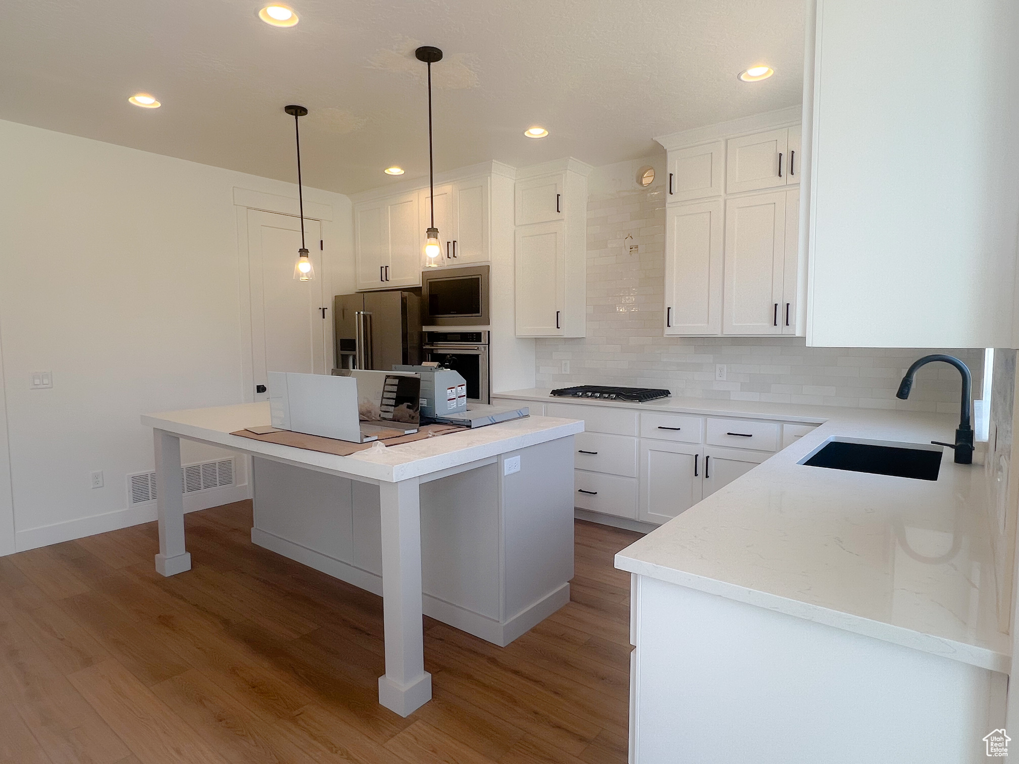 Kitchen with a kitchen breakfast bar, pendant lighting, light hardwood / wood-style floors, sink, and white cabinets