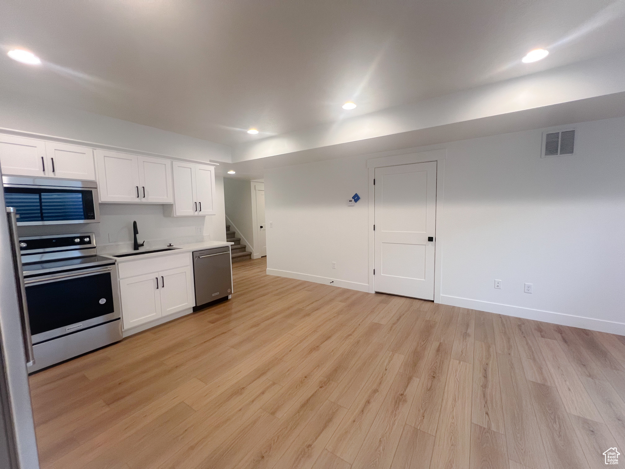 Kitchen with light wood-type flooring, appliances with stainless steel finishes, sink, and white cabinets