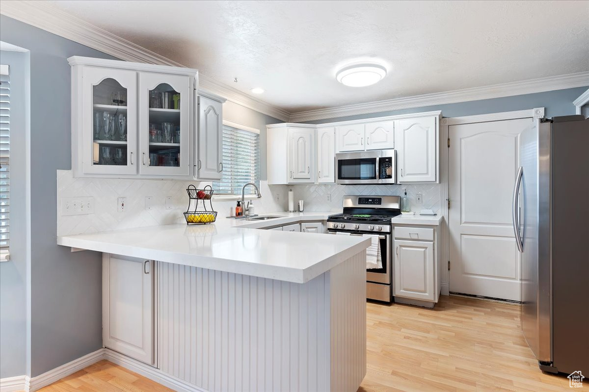 Kitchen featuring white cabinets, light wood-type flooring, stainless steel appliances, sink, and kitchen peninsula