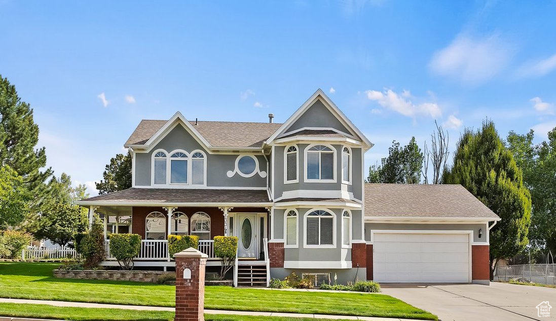 Victorian house featuring a garage, covered porch, and a front lawn