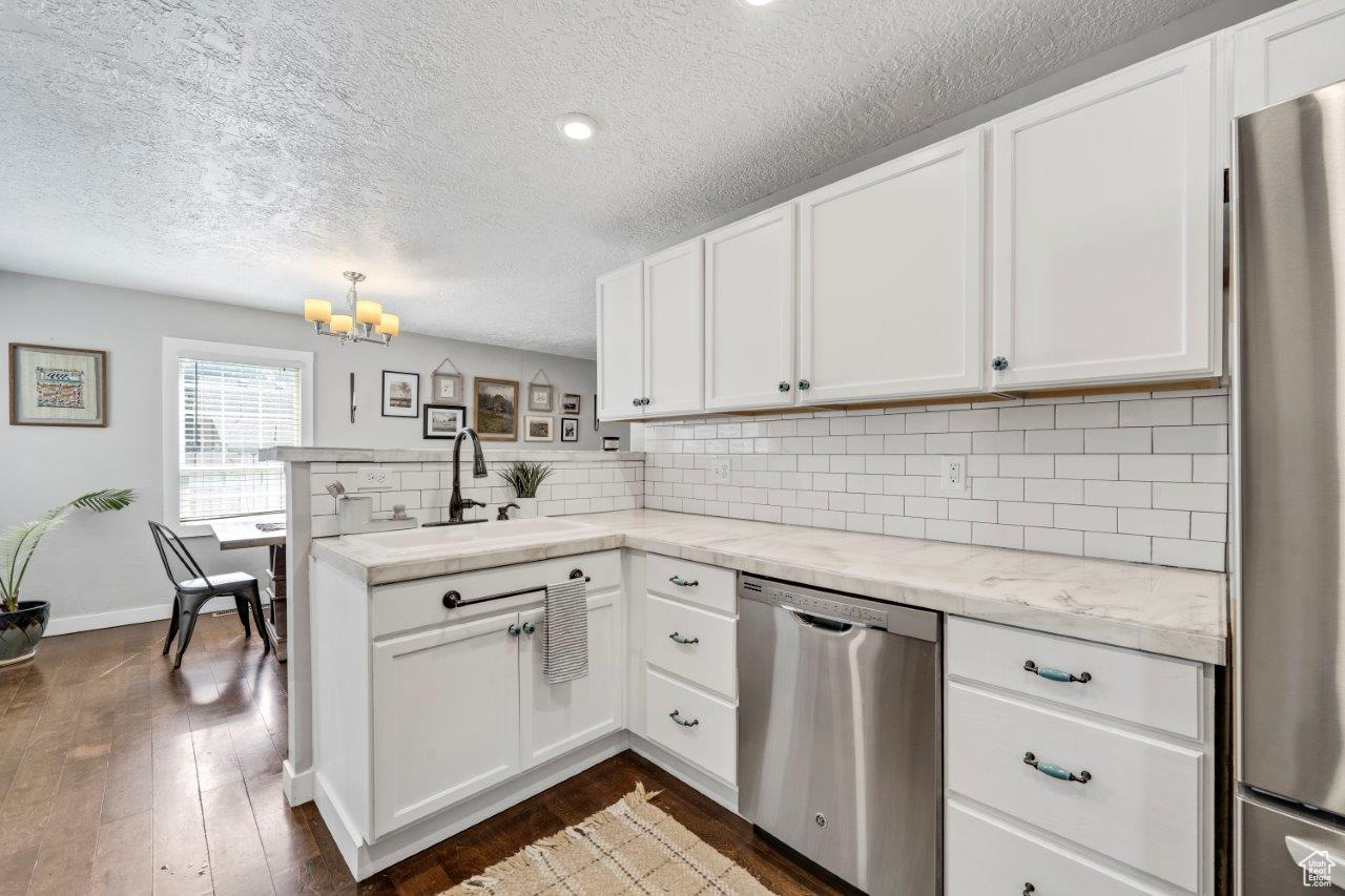 Kitchen with stainless steel appliances, sink, backsplash, and white cabinetry