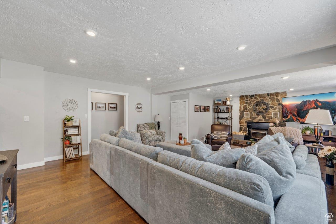 Living room featuring a textured ceiling, wood-type flooring, and a stone fireplace