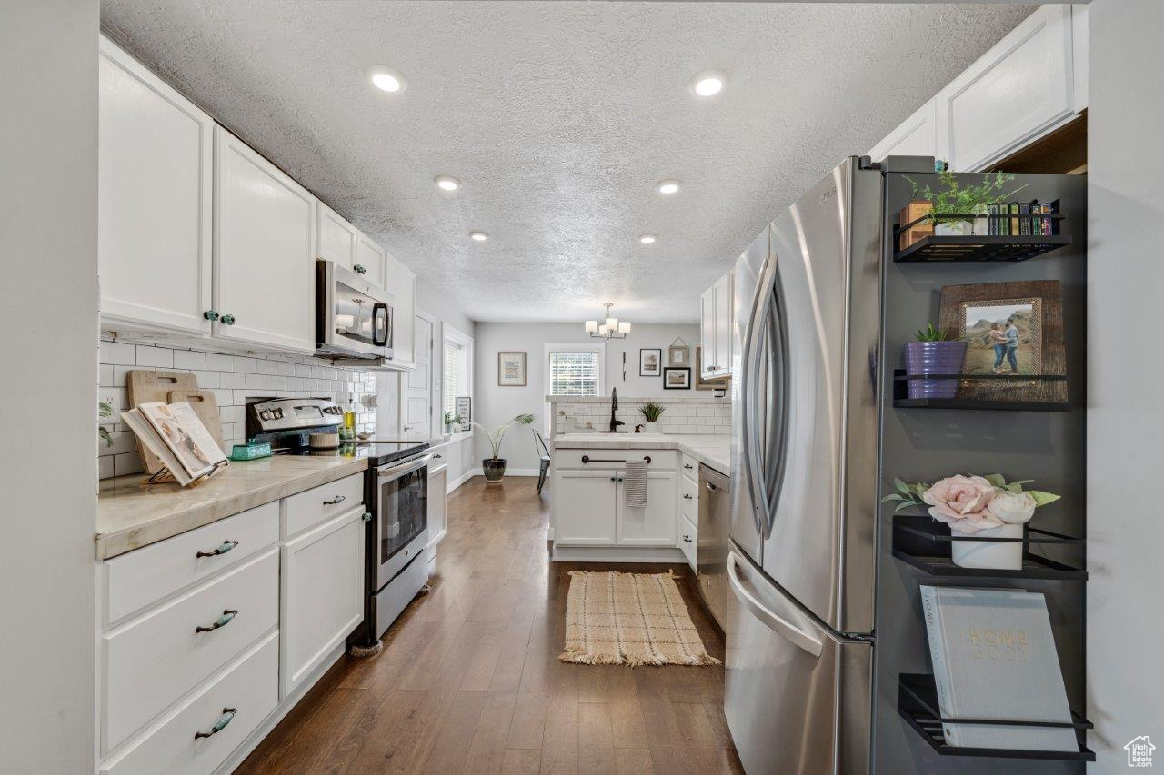 Kitchen featuring a textured ceiling, dark wood-type flooring, appliances with stainless steel finishes, and white cabinets