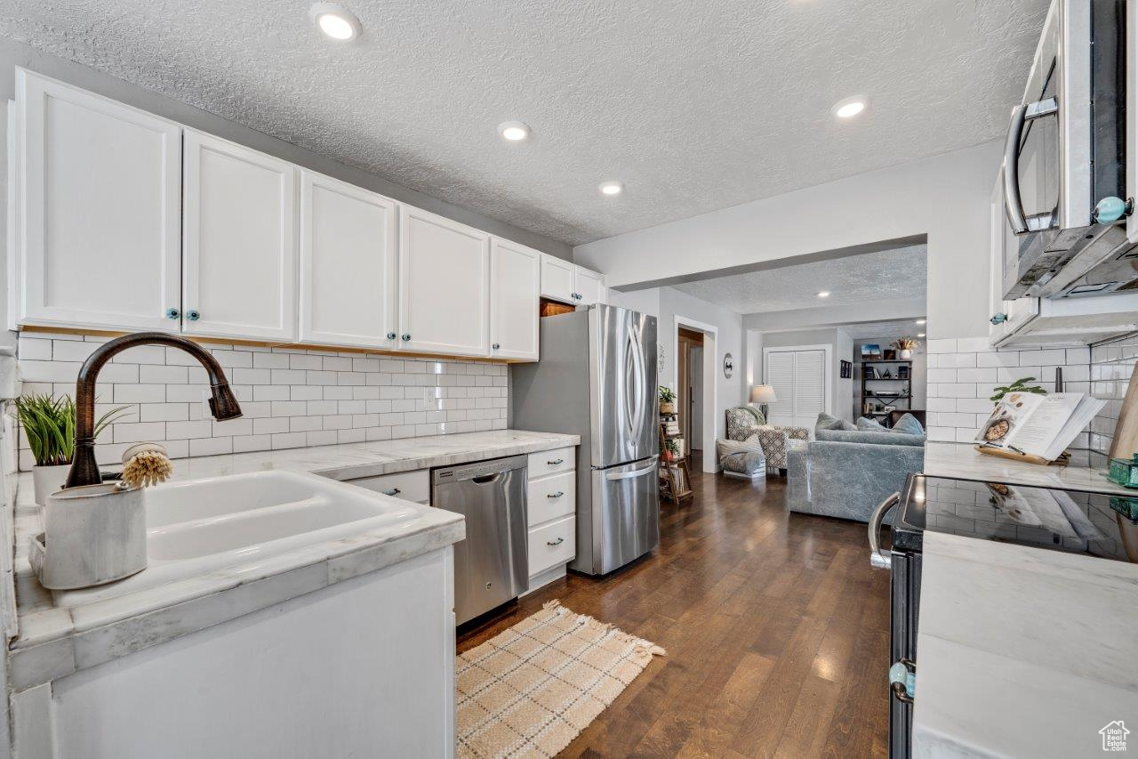 Kitchen with white cabinets, appliances with stainless steel finishes, dark hardwood / wood-style floors, and a textured ceiling