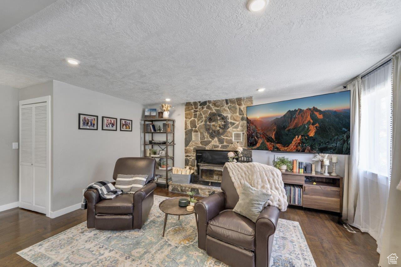 Living room with a textured ceiling, dark wood-type flooring, and a stone fireplace