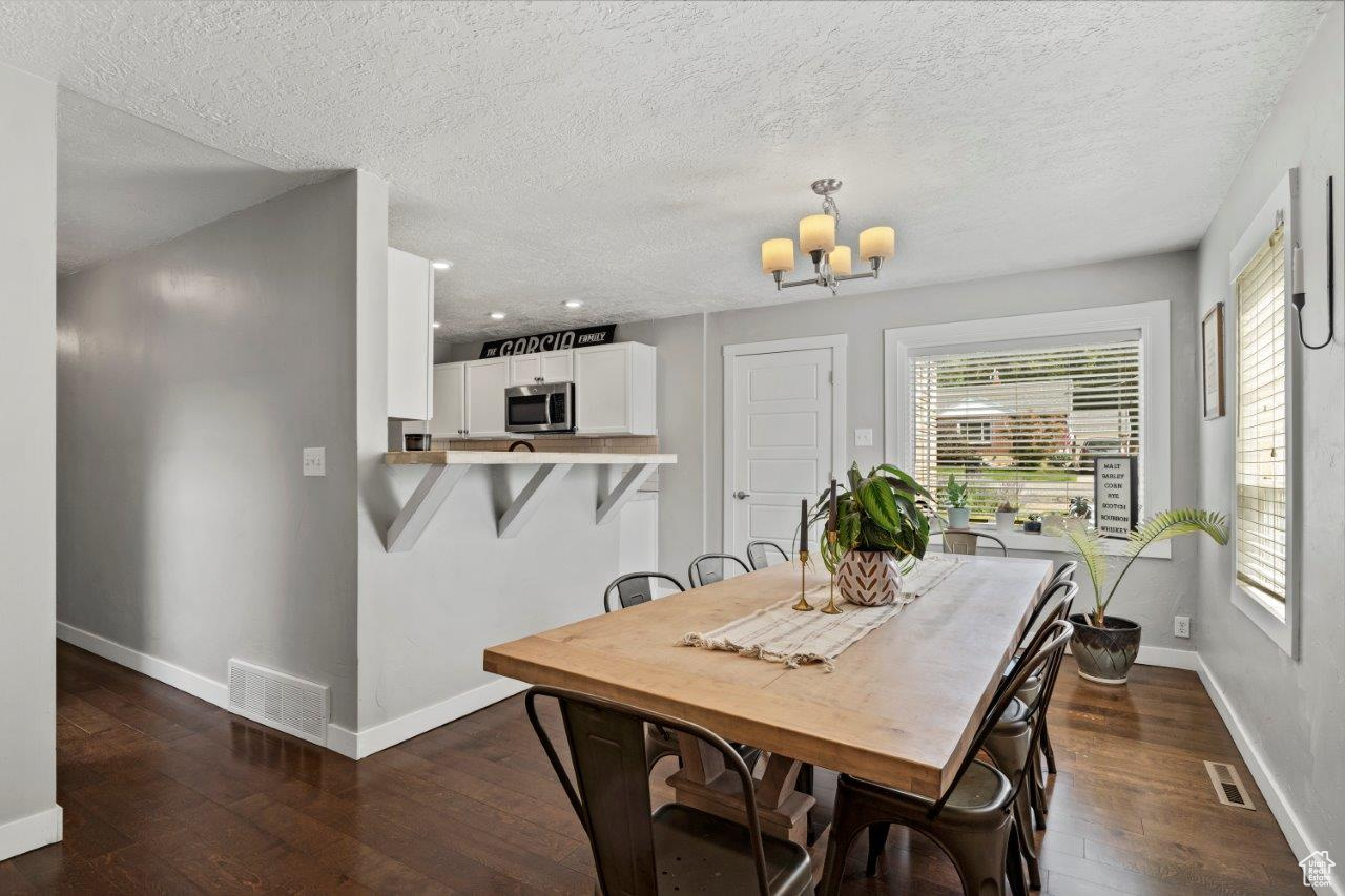 Dining area with dark hardwood / wood-style flooring, an inviting chandelier, and a textured ceiling