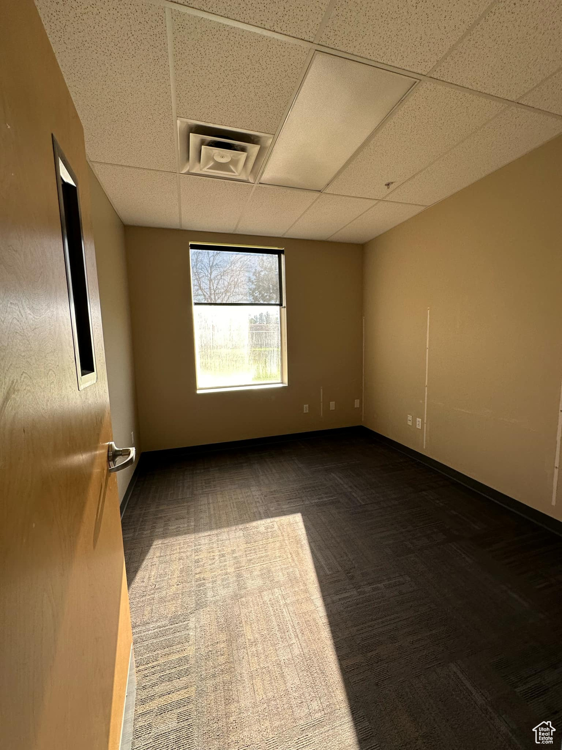 Unfurnished room featuring dark colored carpet and a drop ceiling