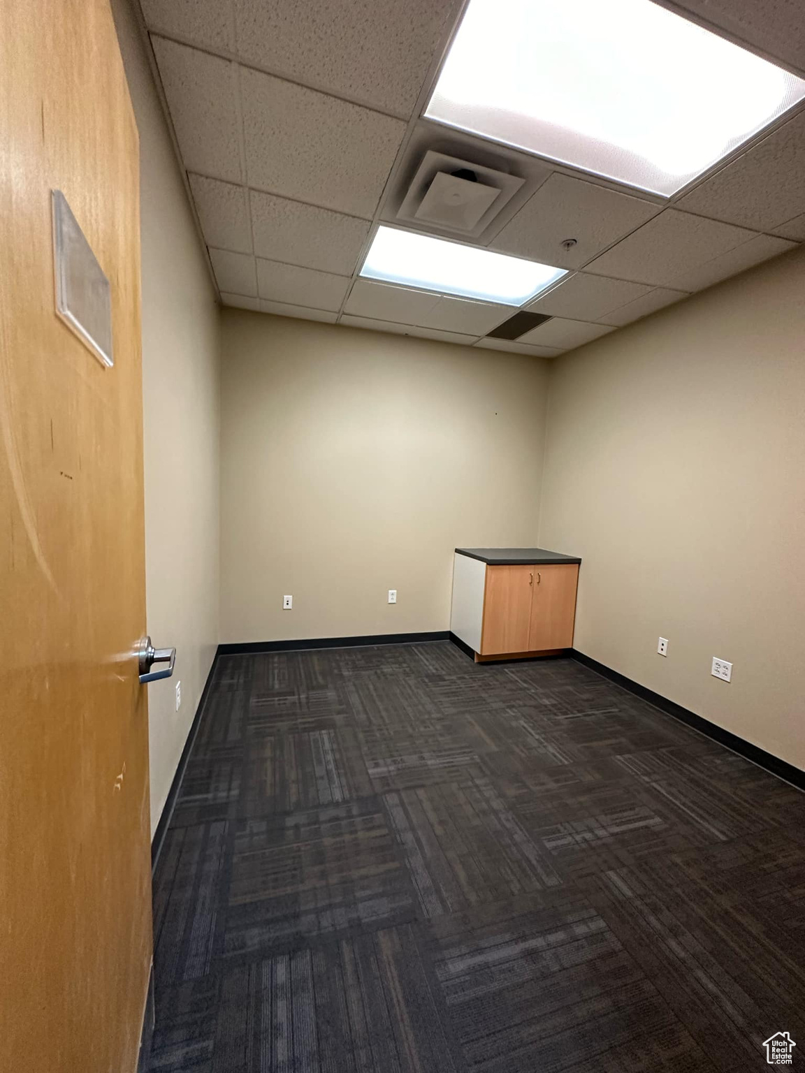 Unfurnished room featuring a paneled ceiling and dark colored carpet