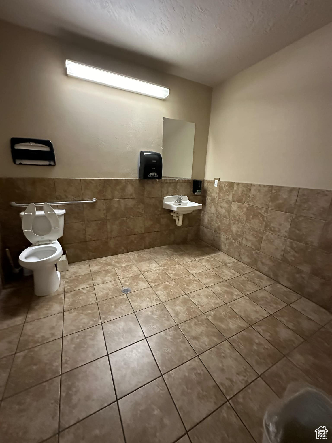 Bathroom with tile patterned floors, toilet, sink, tile walls, and a textured ceiling