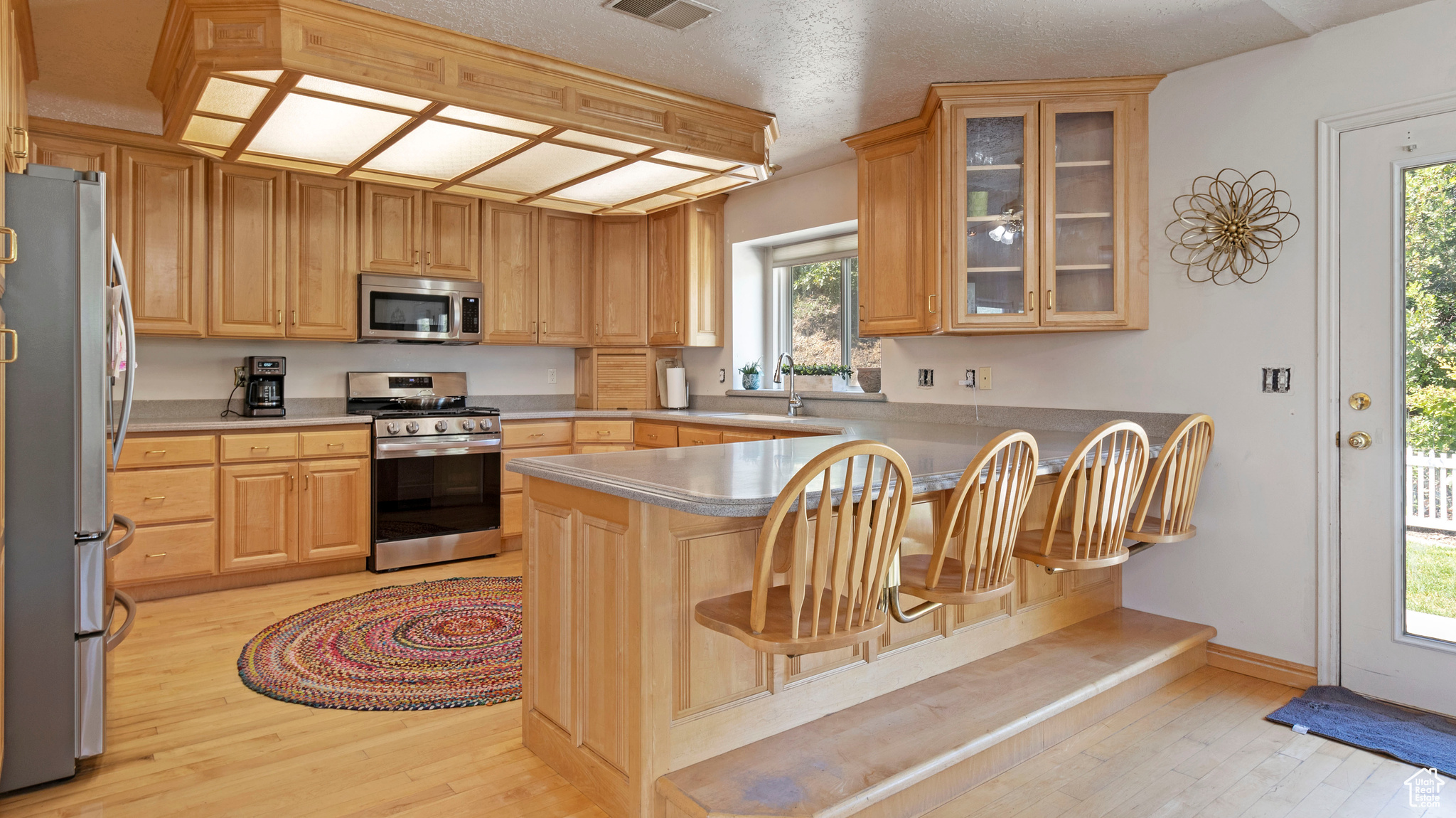 Kitchen featuring a textured ceiling, light hardwood / wood-style flooring, a breakfast bar, kitchen peninsula, and stainless steel appliances