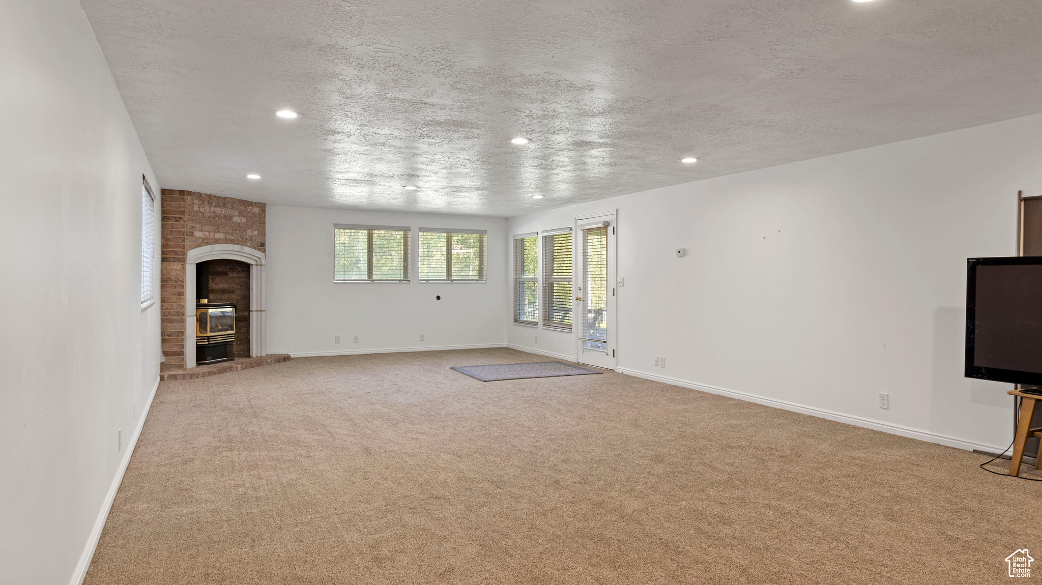 Unfurnished living room featuring light colored carpet, a fireplace, and a textured ceiling