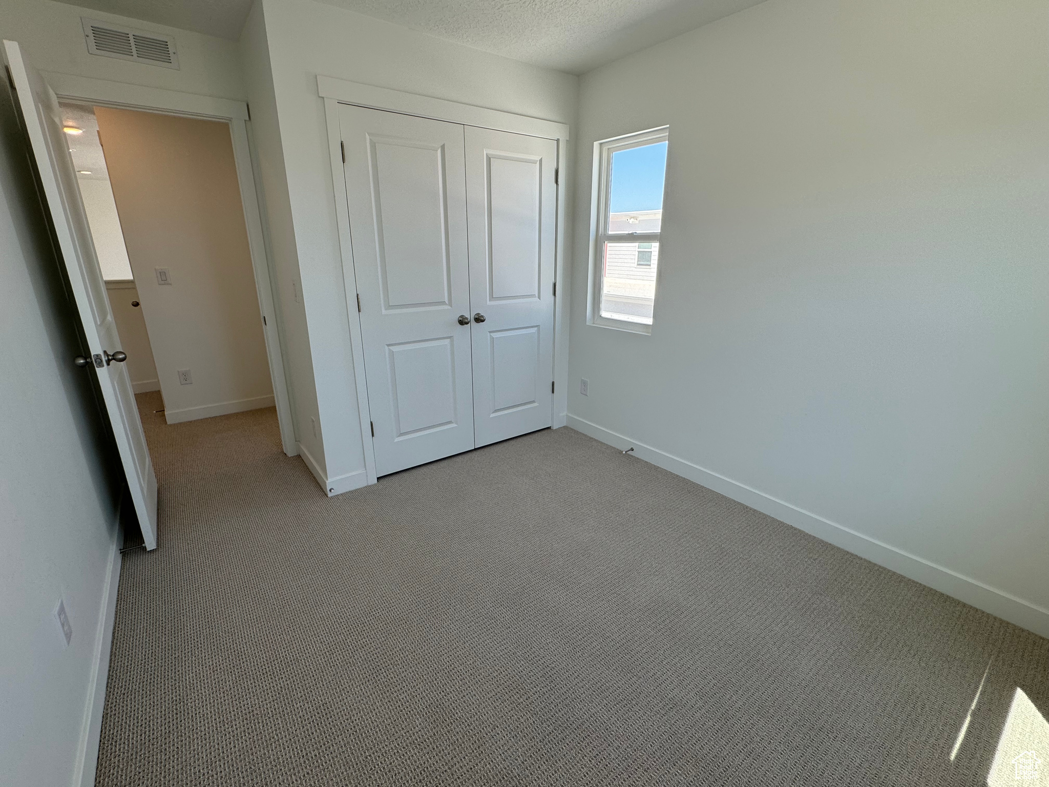 Unfurnished bedroom featuring light carpet, a textured ceiling, and a closet