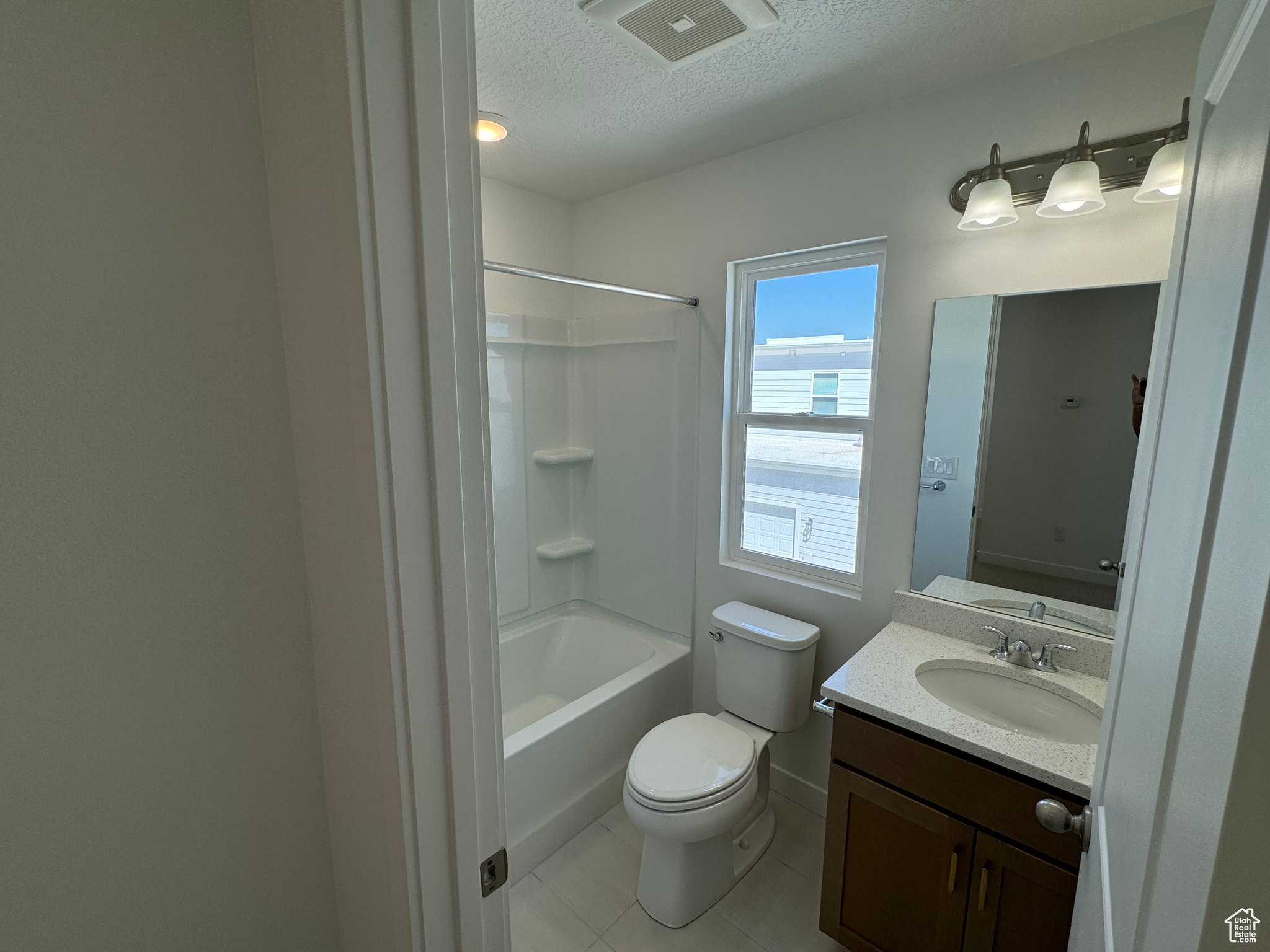 Full bathroom with a textured ceiling, vanity, tile patterned flooring, toilet, and shower / bathing tub combination