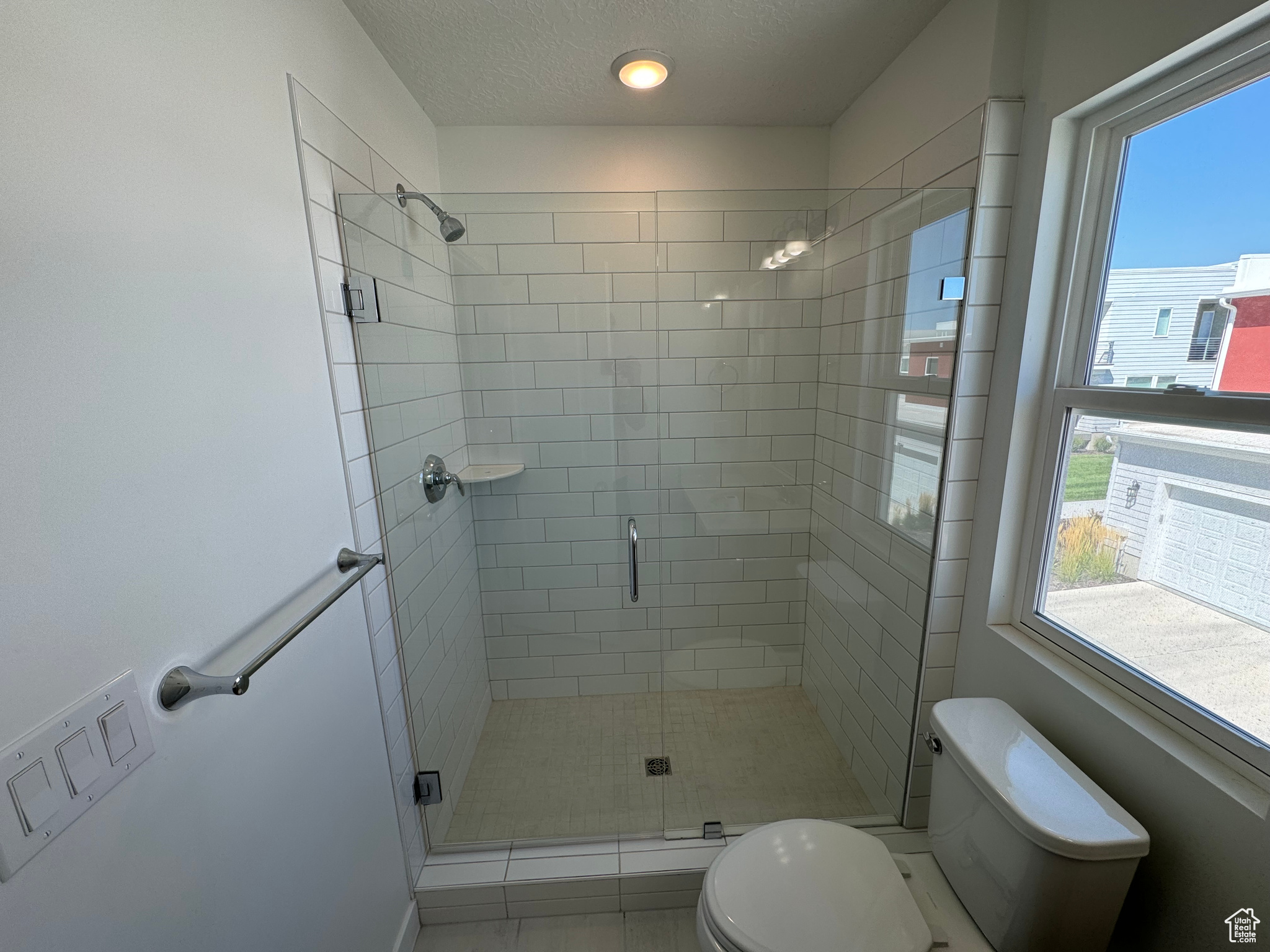 Bathroom featuring a textured ceiling, a healthy amount of sunlight, toilet, and a shower with shower door