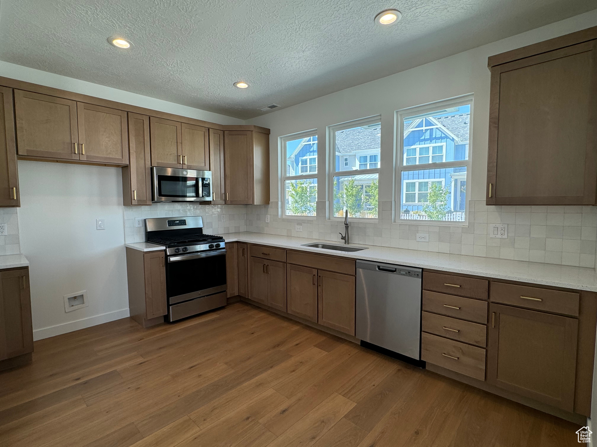 Kitchen with a textured ceiling, light hardwood / wood-style flooring, stainless steel appliances, sink, and decorative backsplash