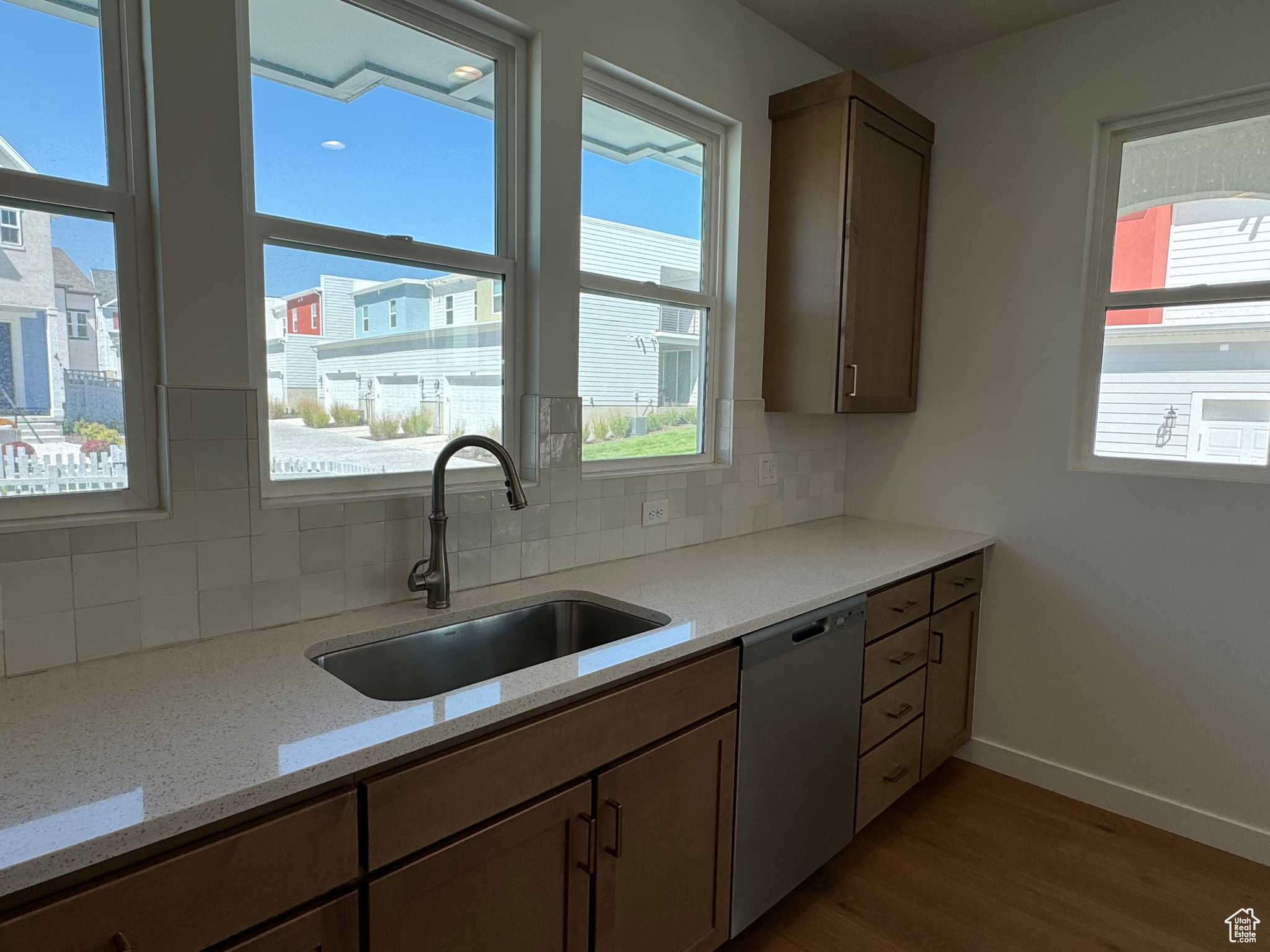 Kitchen featuring dishwasher, hardwood / wood-style floors, light stone counters, sink, and tasteful backsplash