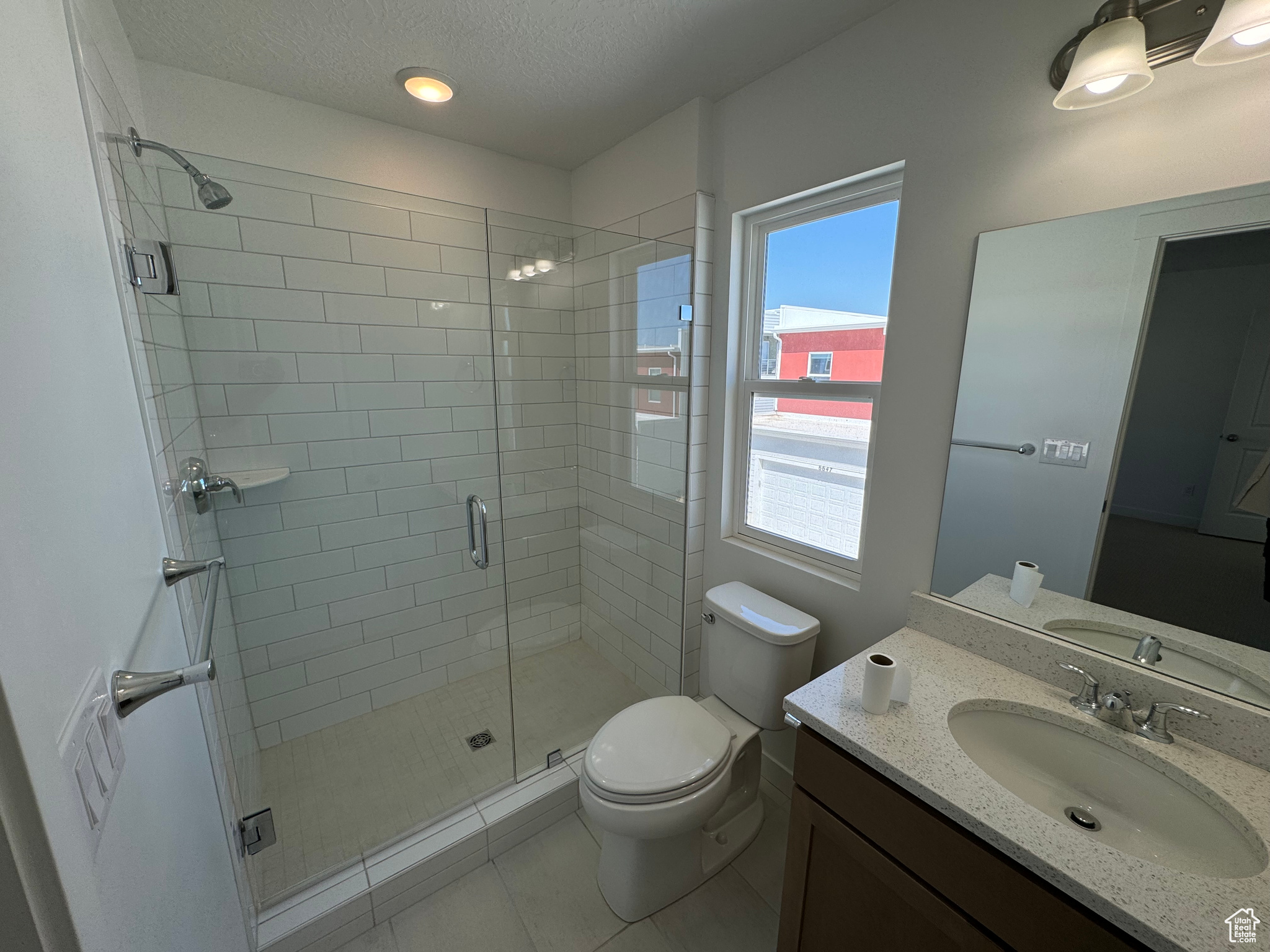 Bathroom featuring tile patterned flooring, an enclosed shower, toilet, vanity, and a textured ceiling