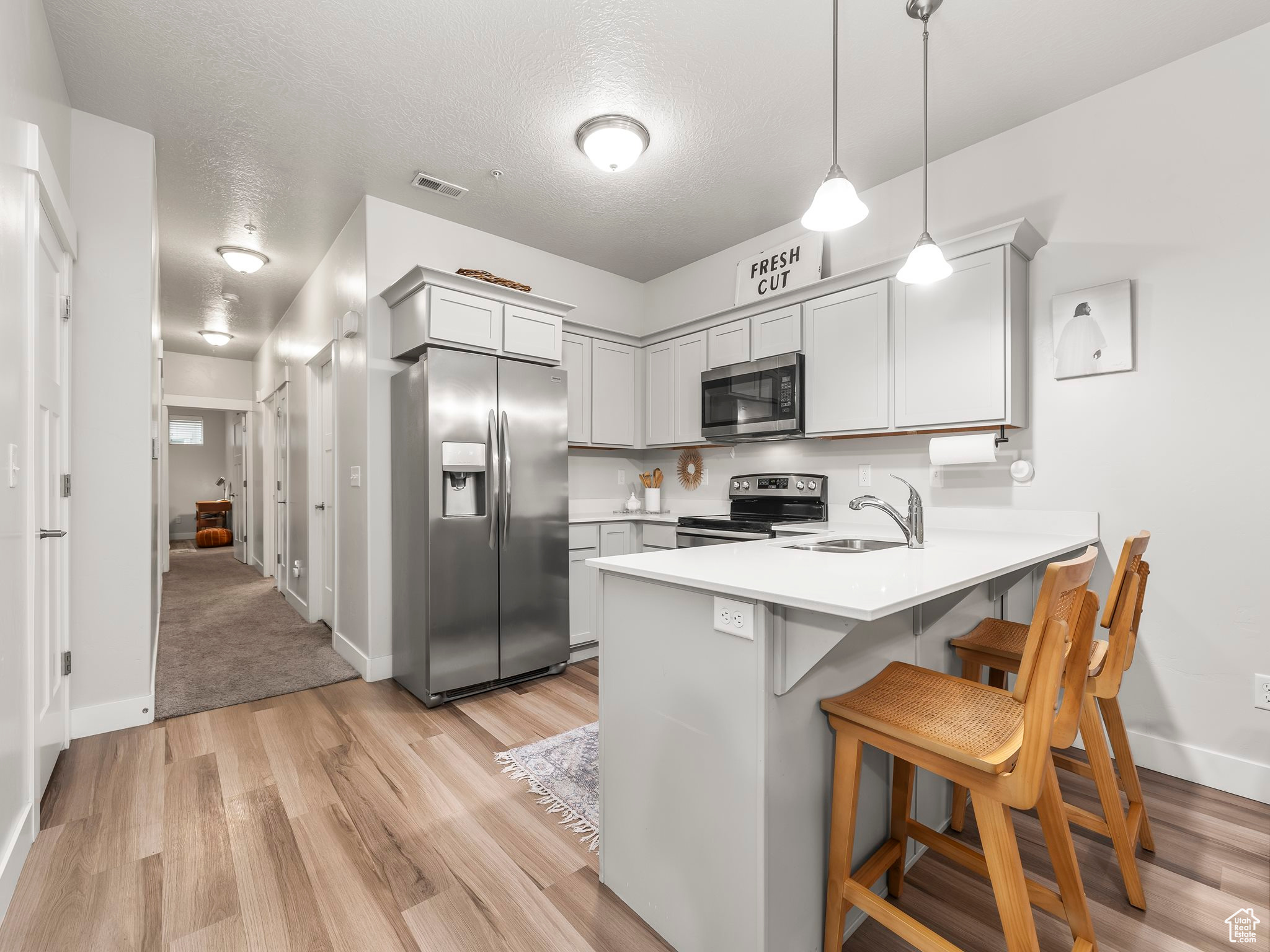 Kitchen featuring light wood-type flooring, appliances with stainless steel finishes, sink, kitchen peninsula, and a kitchen bar