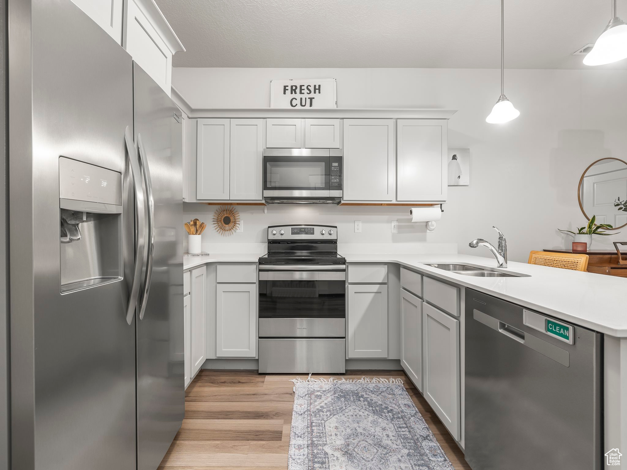 Kitchen with hanging light fixtures, appliances with stainless steel finishes, light hardwood / wood-style floors, sink, and kitchen peninsula