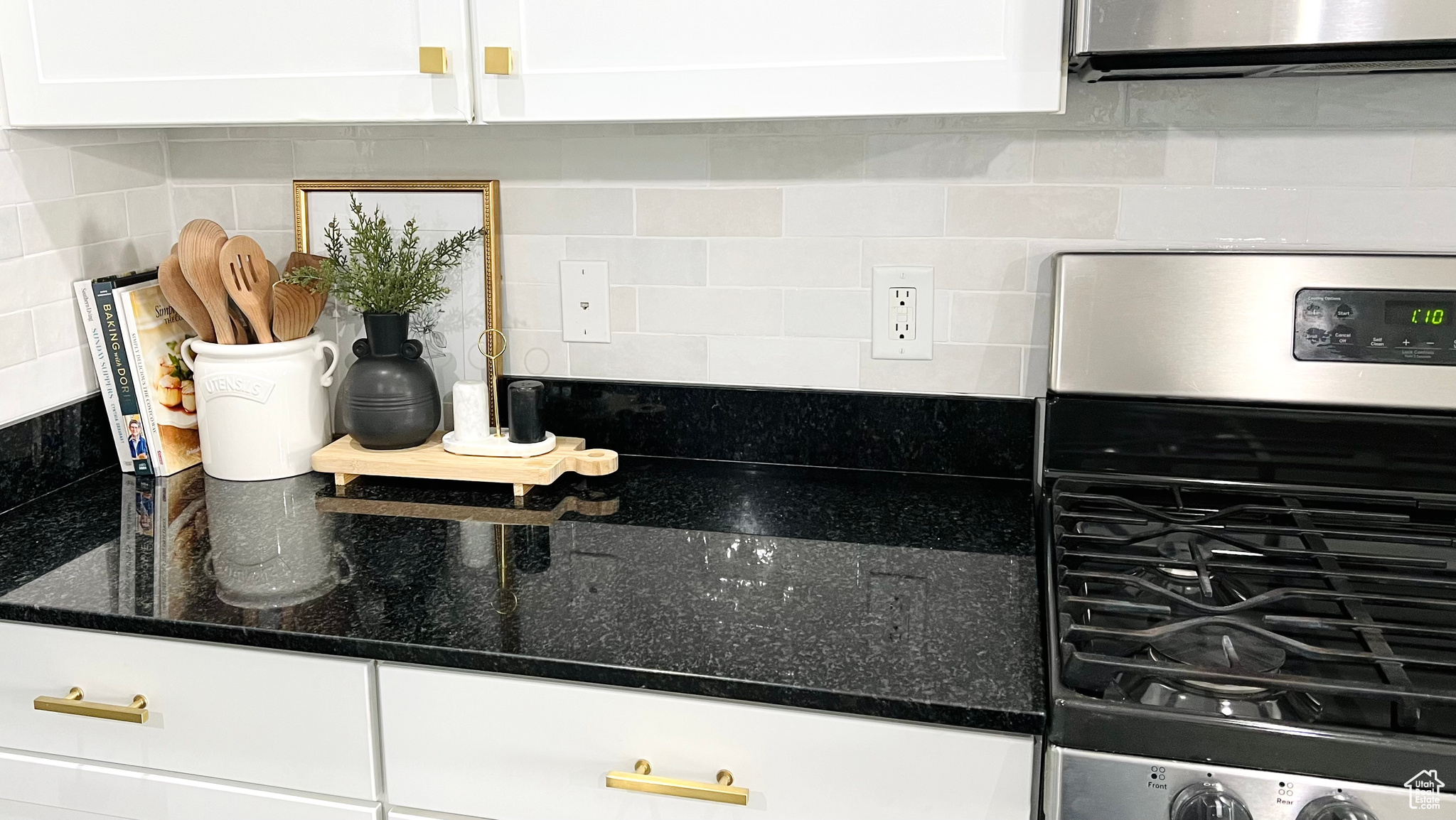 Kitchen with dark stone countertops, decorative Bedrosians Cloe tile backsplash, stainless steel gas stove, and white cabinets