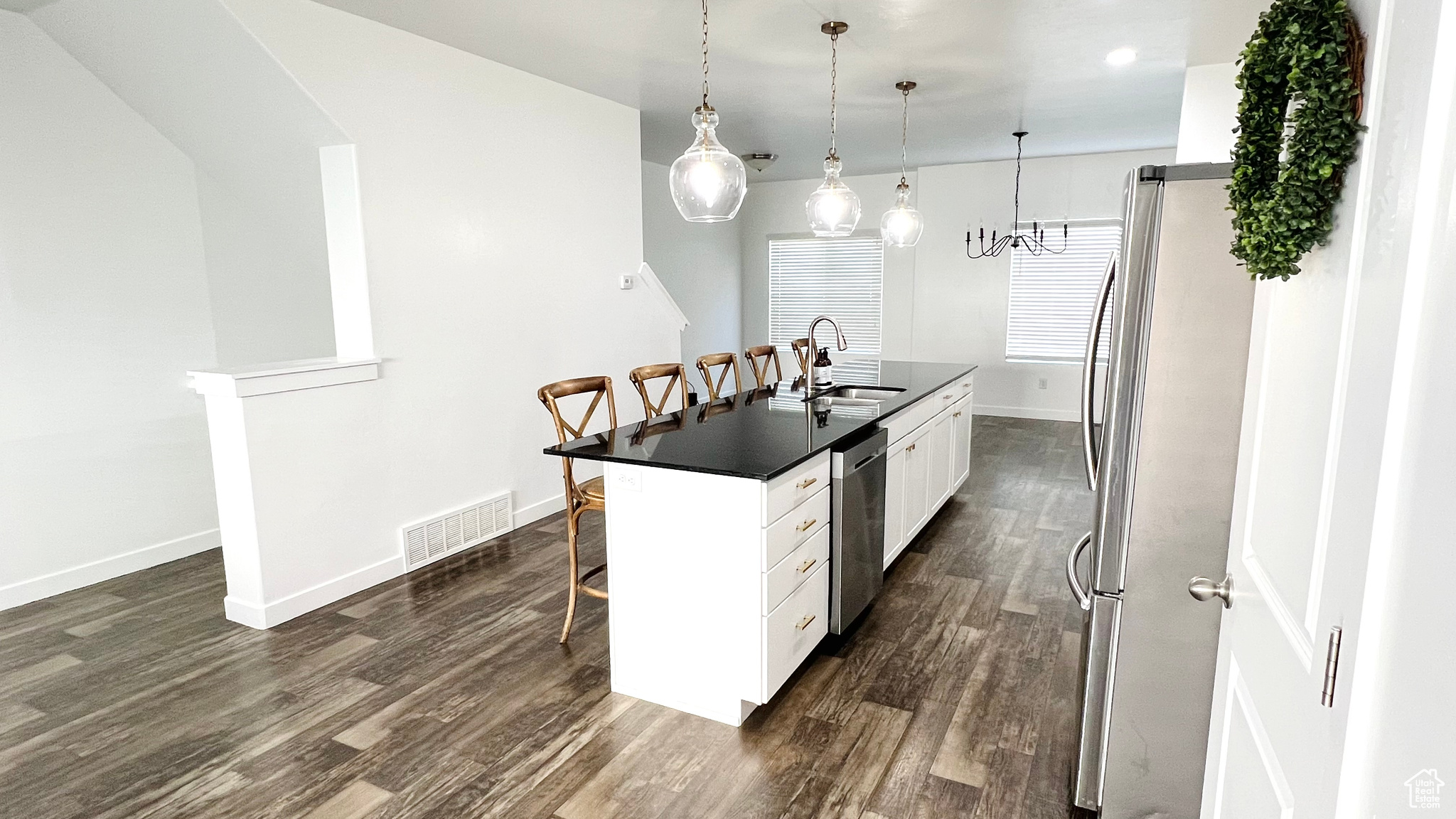 Kitchen featuring pendant lighting, a kitchen island with sink, white cabinets, appliances with stainless steel finishes, and a kitchen bar