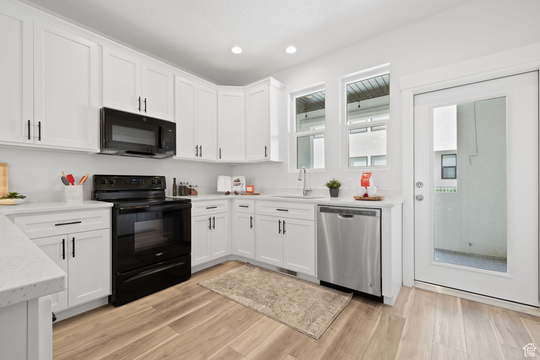 Kitchen featuring black appliances, sink, light hardwood / wood-style flooring, and white cabinetry