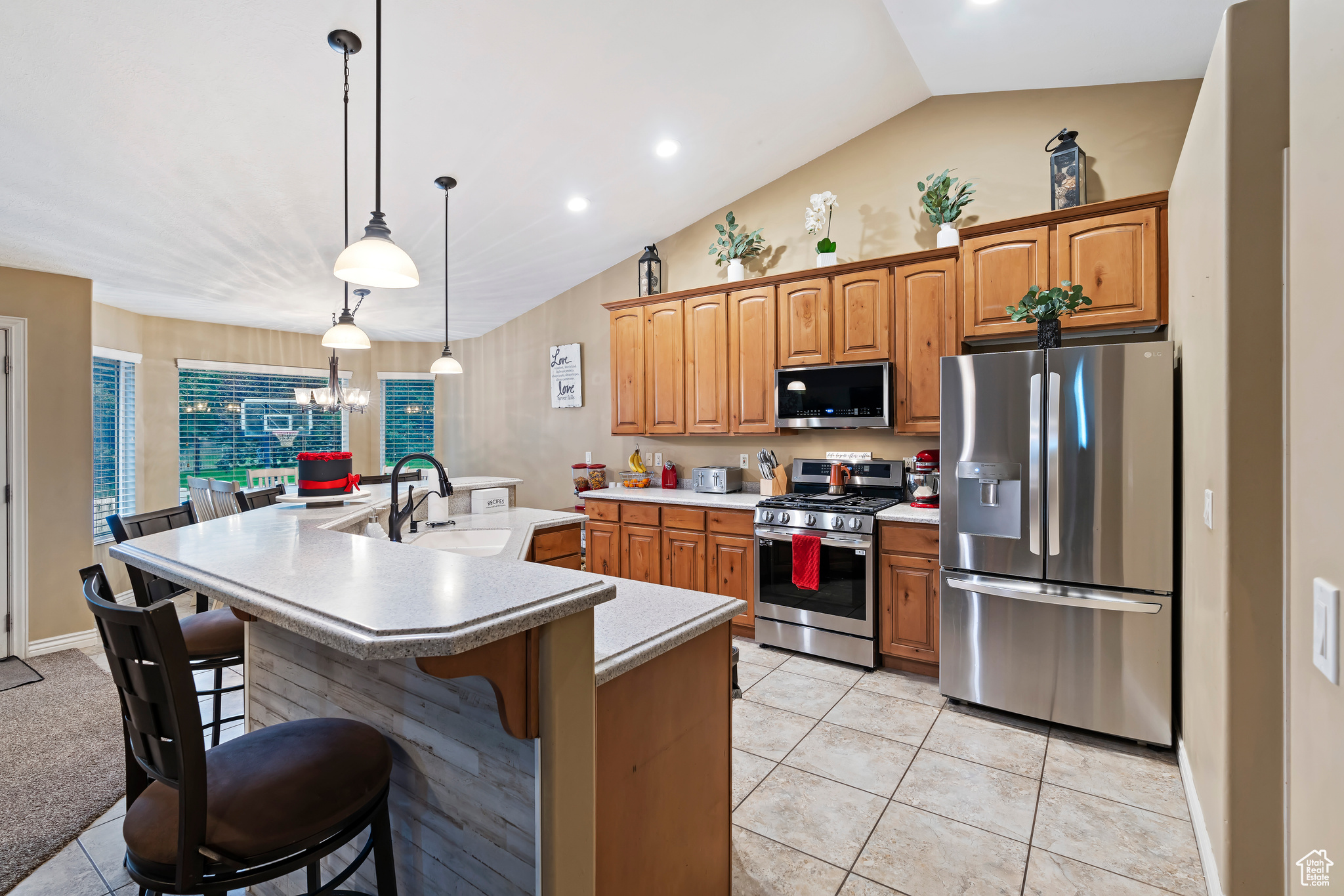 Kitchen with a breakfast bar, stainless steel appliances, decorative light fixtures, a center island with sink, and sink