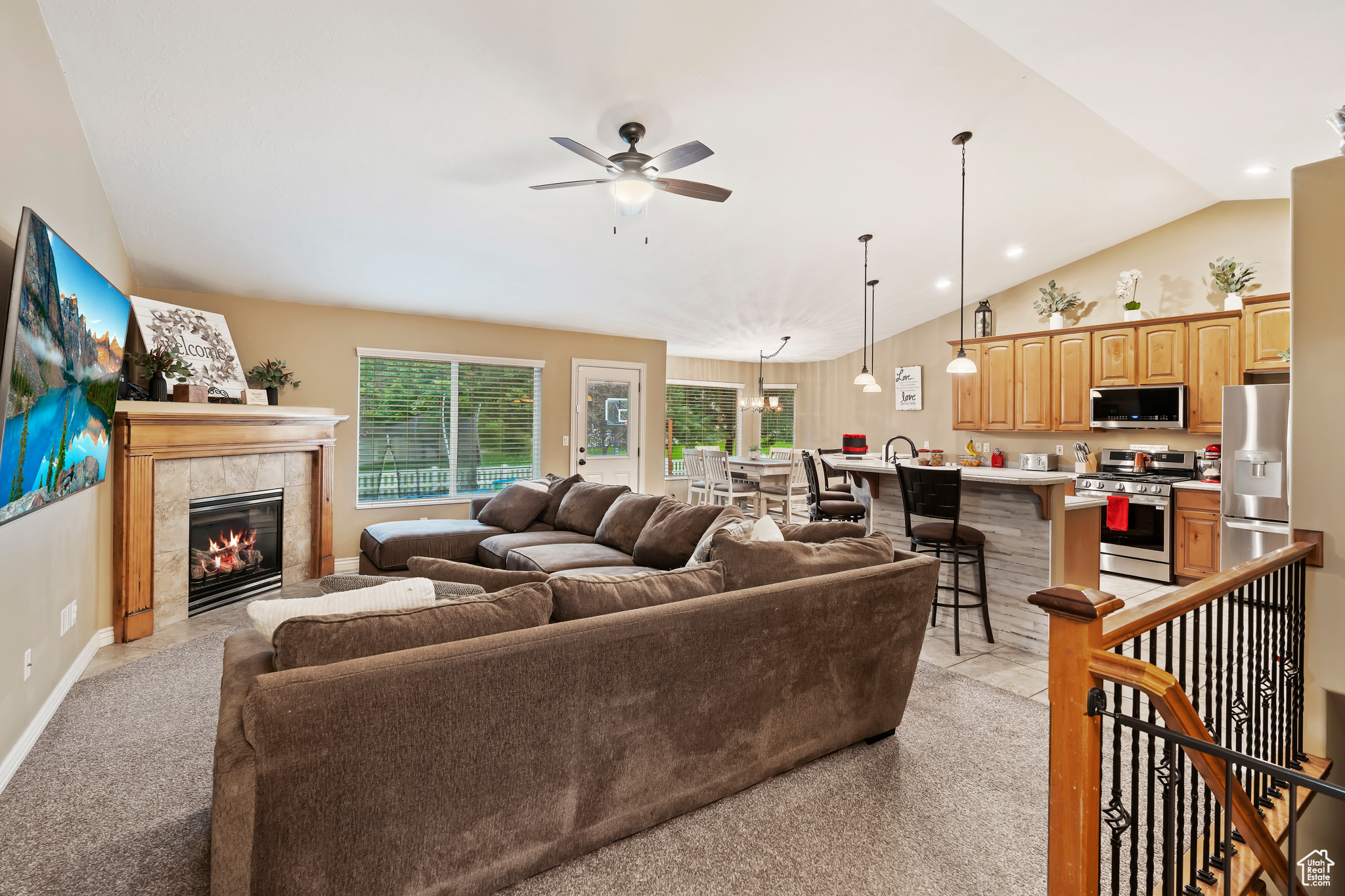 Carpeted living room featuring a tile fireplace, lofted ceiling, and ceiling fan