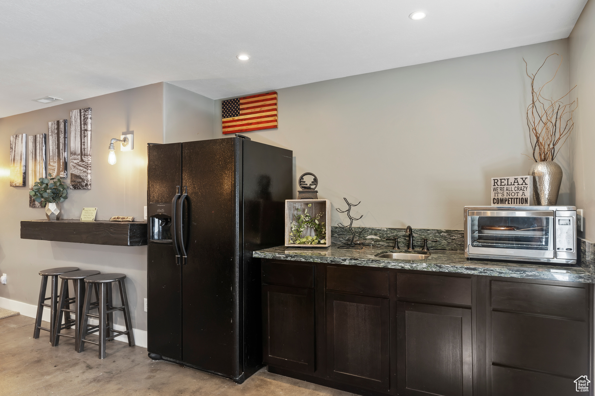 Kitchen featuring dark stone countertops, black fridge, dark brown cabinetry, and sink