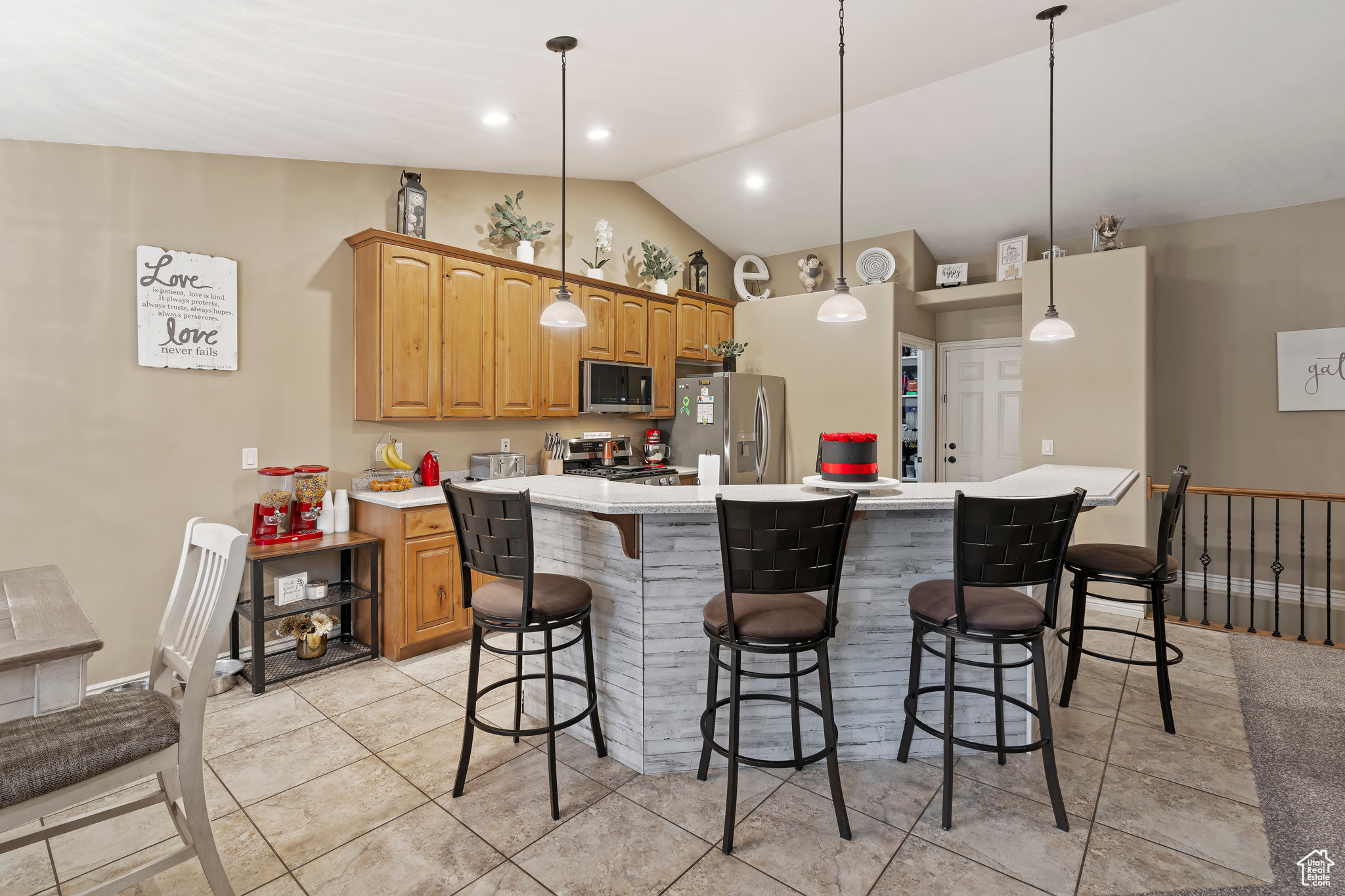 Kitchen featuring pendant lighting, lofted ceiling, a center island, appliances with stainless steel finishes, and a breakfast bar