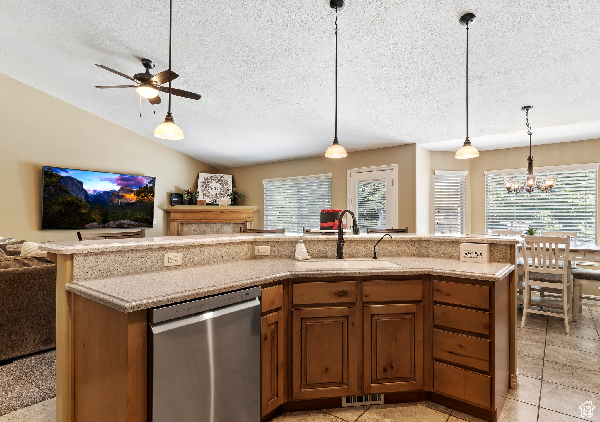 Kitchen featuring ceiling fan with notable chandelier, dishwasher, lofted ceiling, decorative light fixtures, and a kitchen island with sink