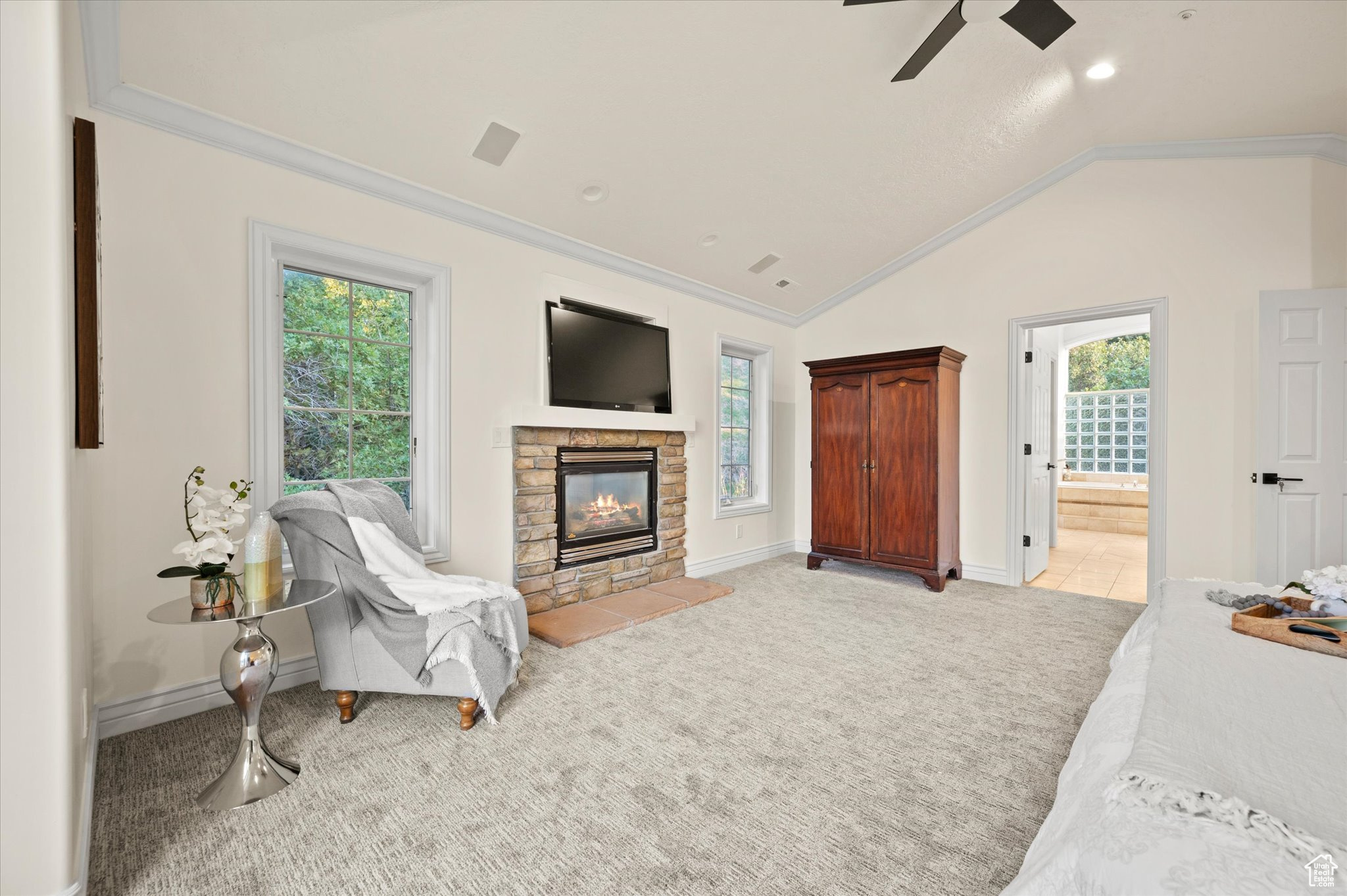 Living room featuring crown molding, a healthy amount of sunlight, ceiling fan, and a stone fireplace