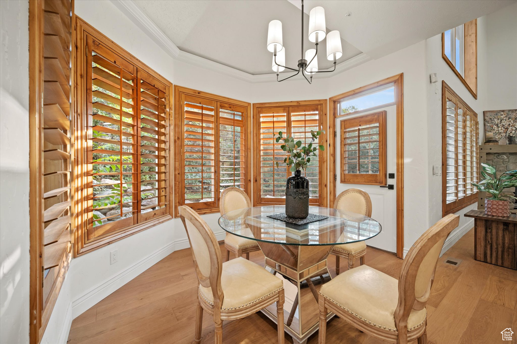 Dining room with ornamental molding, a notable chandelier, a tray ceiling, and light hardwood / wood-style floors