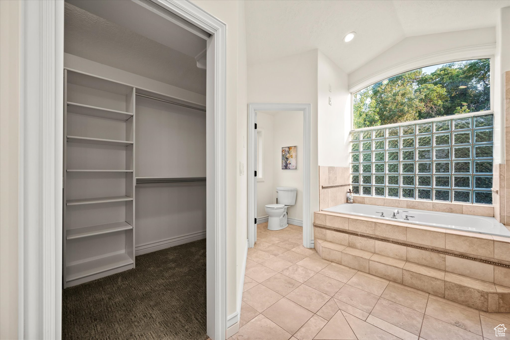 Bathroom featuring vaulted ceiling, toilet, a relaxing tiled tub, and tile patterned flooring