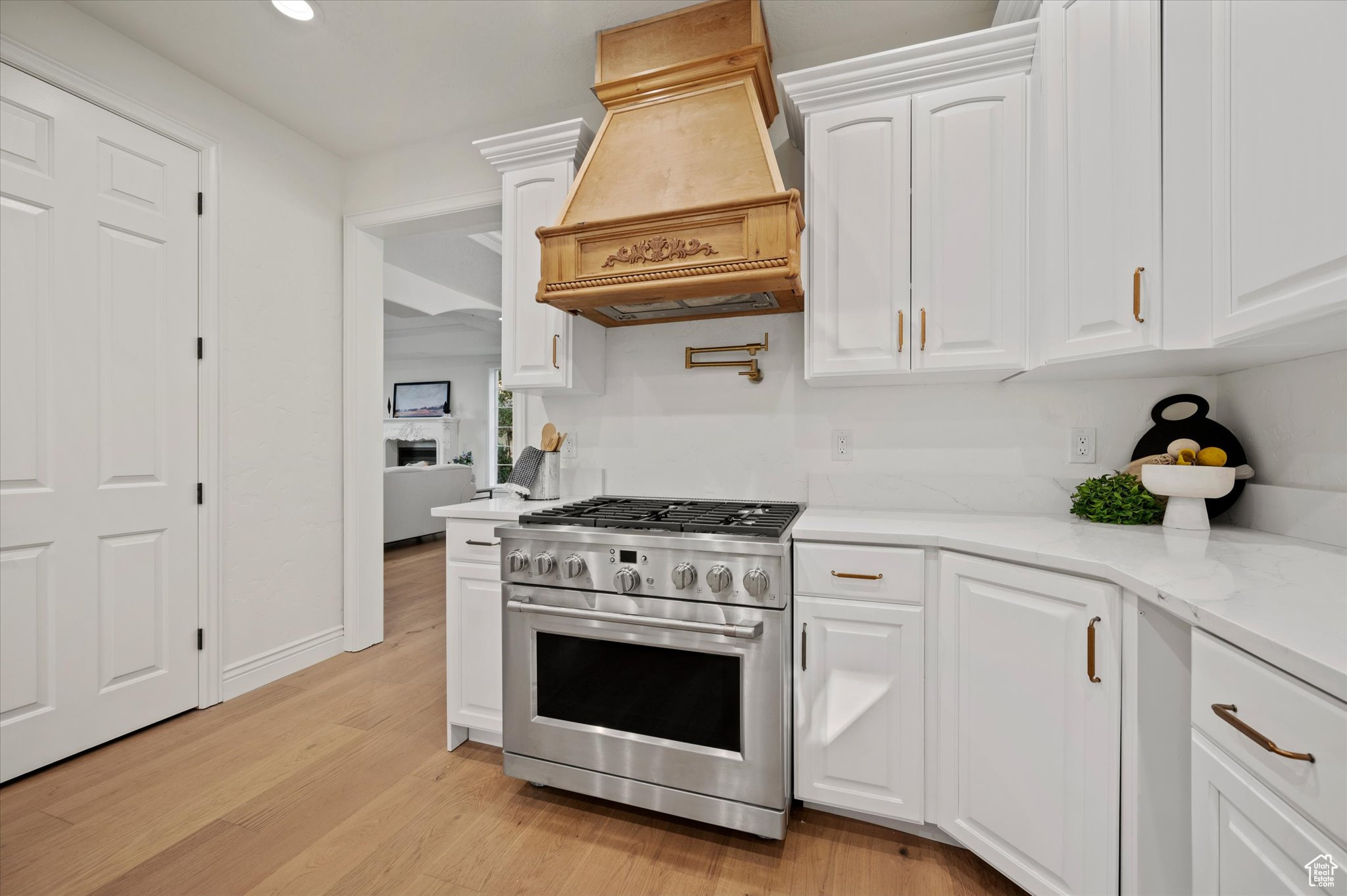 Kitchen with light wood-type flooring, custom exhaust hood, white cabinetry, light stone counters, and high end stove