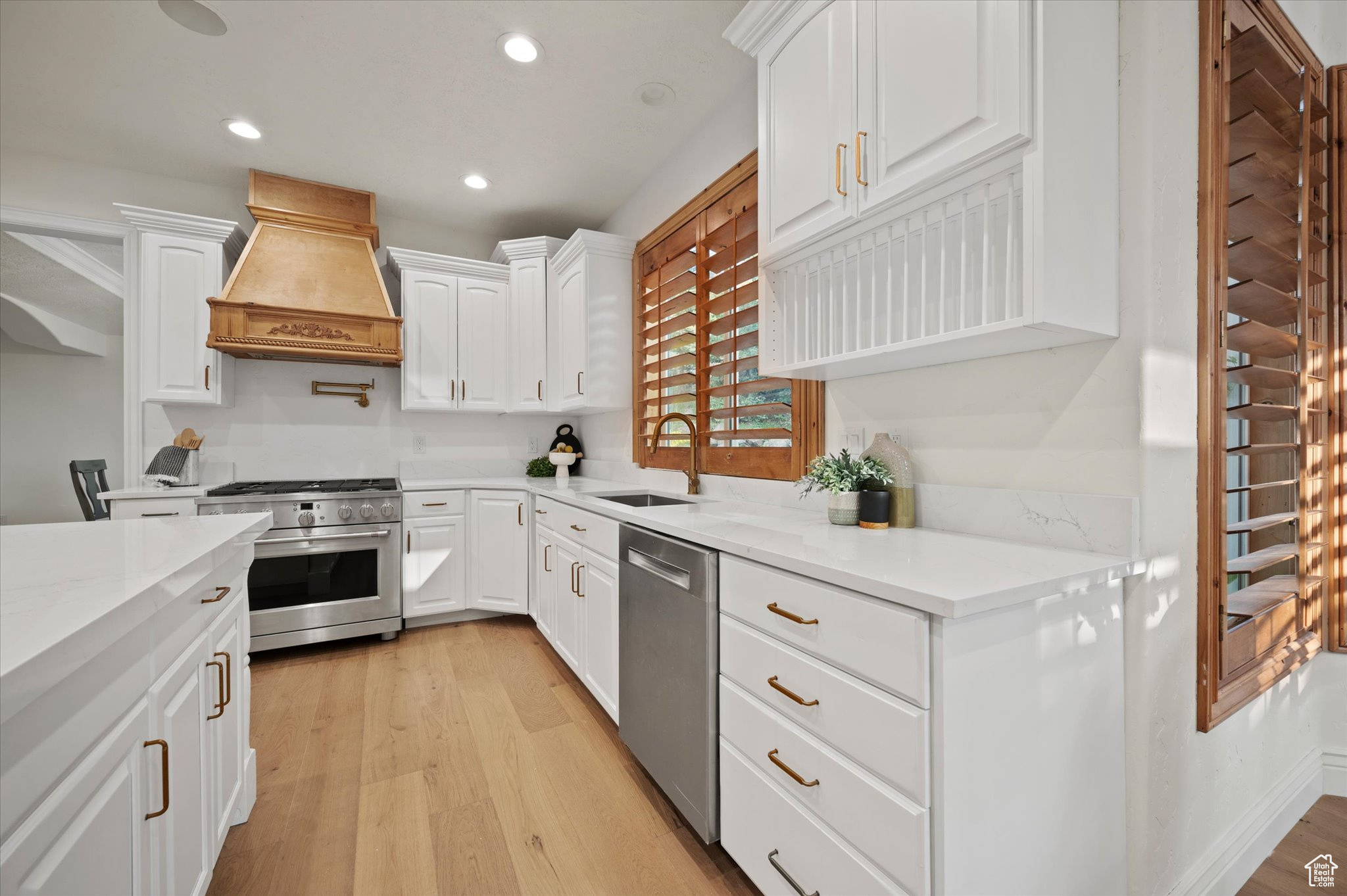 Kitchen with appliances with stainless steel finishes, light hardwood / wood-style floors, white cabinetry, sink, and premium range hood