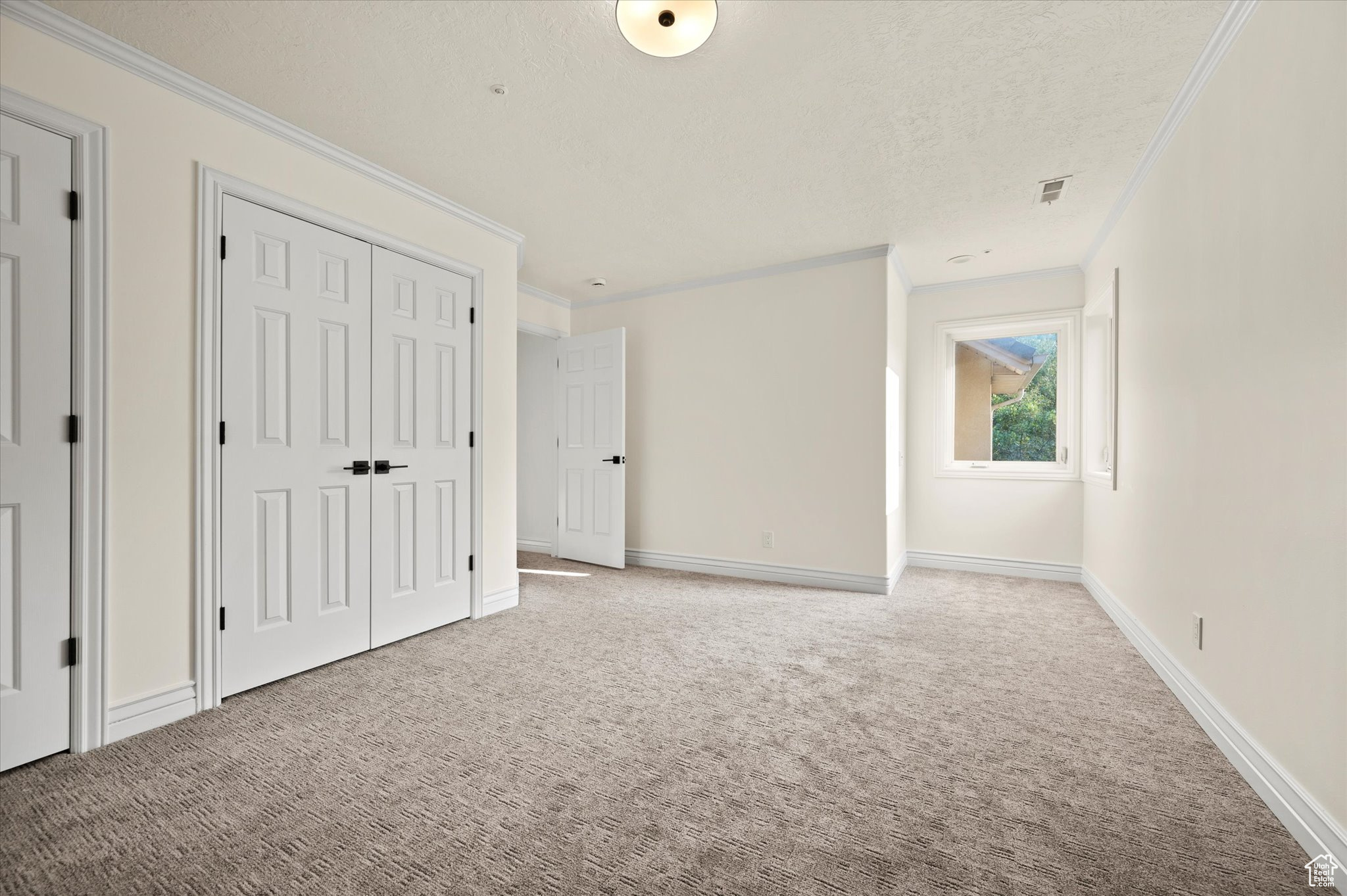 Unfurnished bedroom featuring light colored carpet, a textured ceiling, and ornamental molding