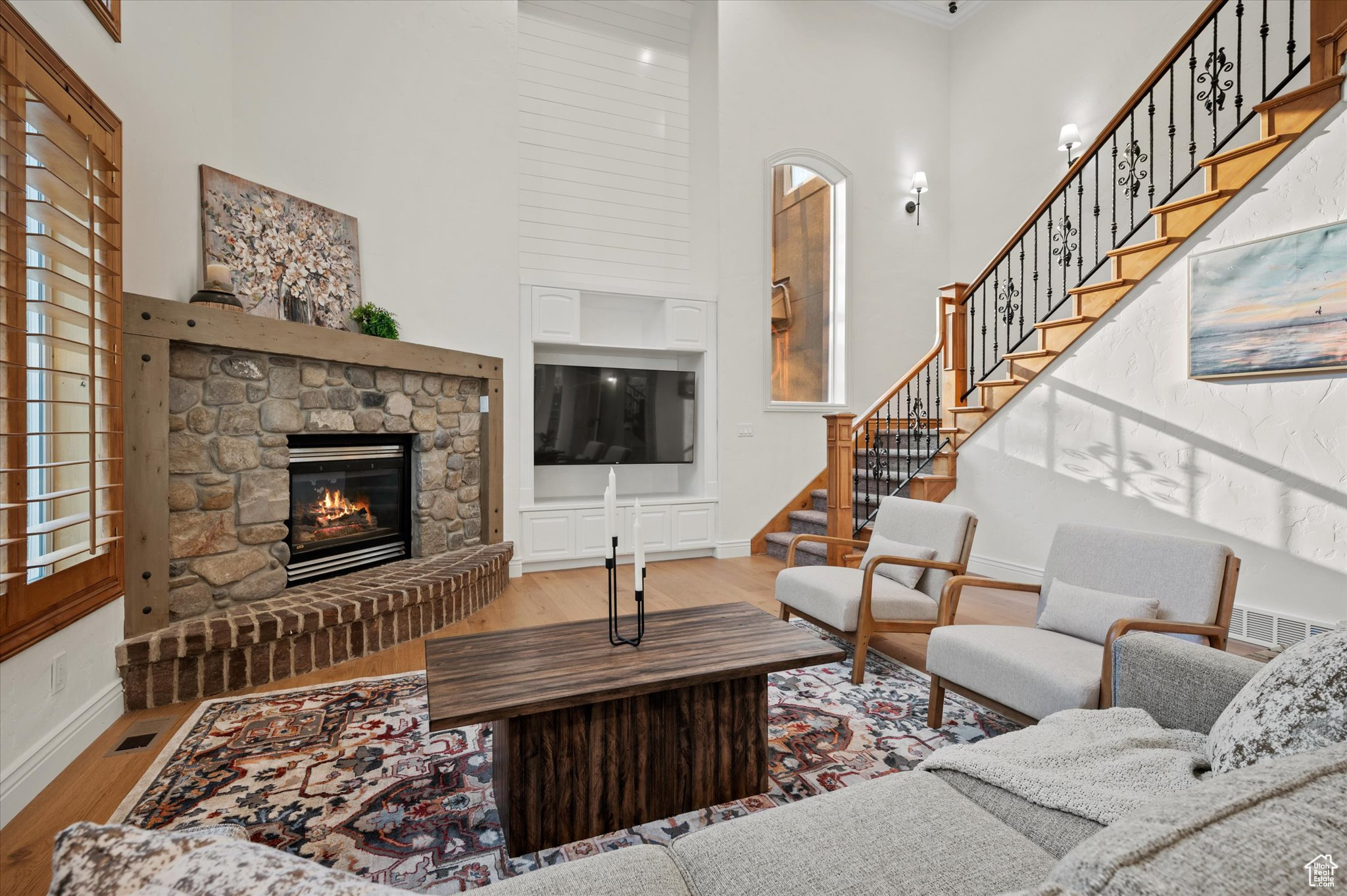 Living room with a towering ceiling, wood-type flooring, crown molding, and a stone fireplace