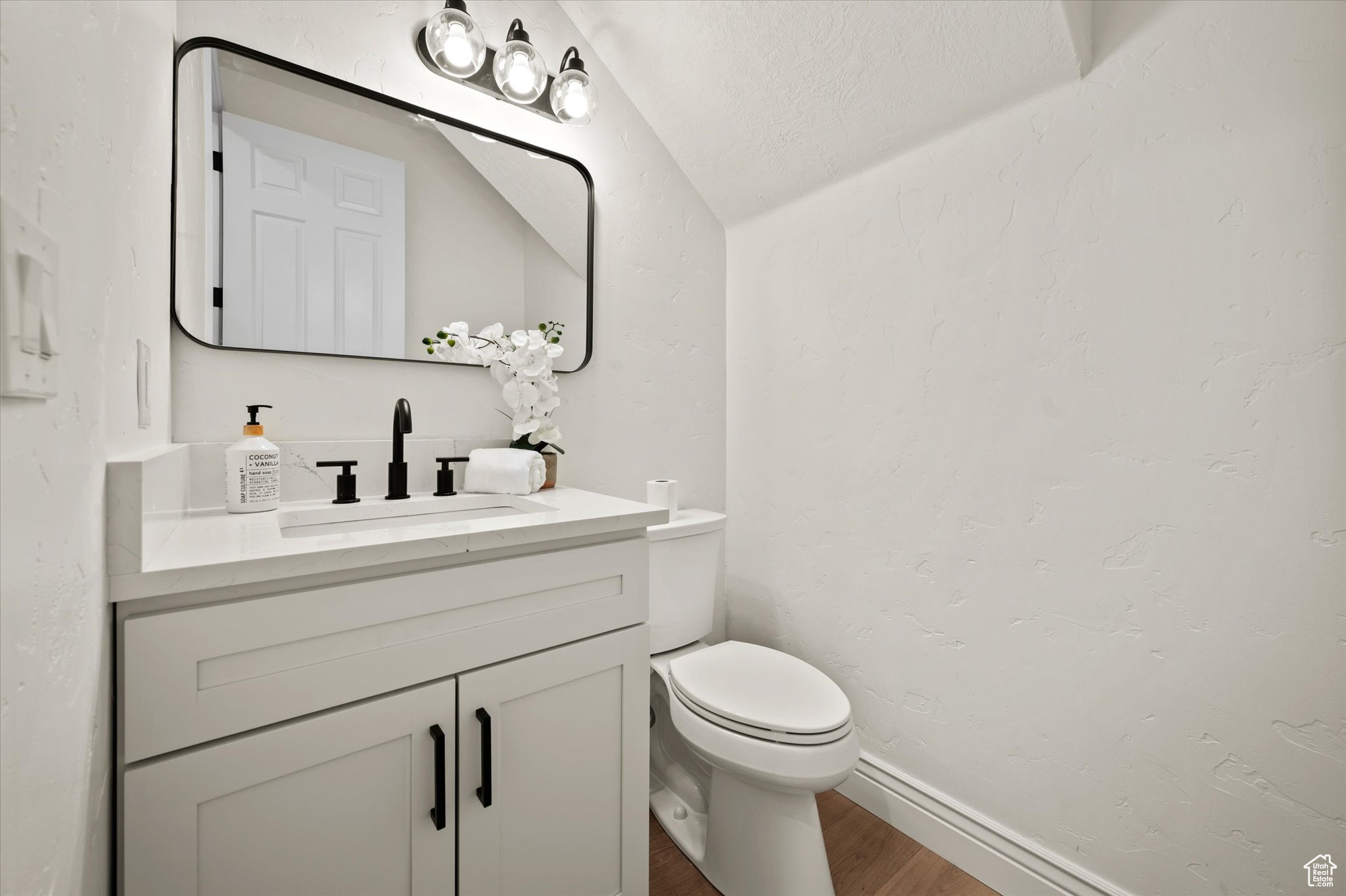 Bathroom featuring a textured ceiling, vanity, vaulted ceiling, wood-type flooring, and toilet