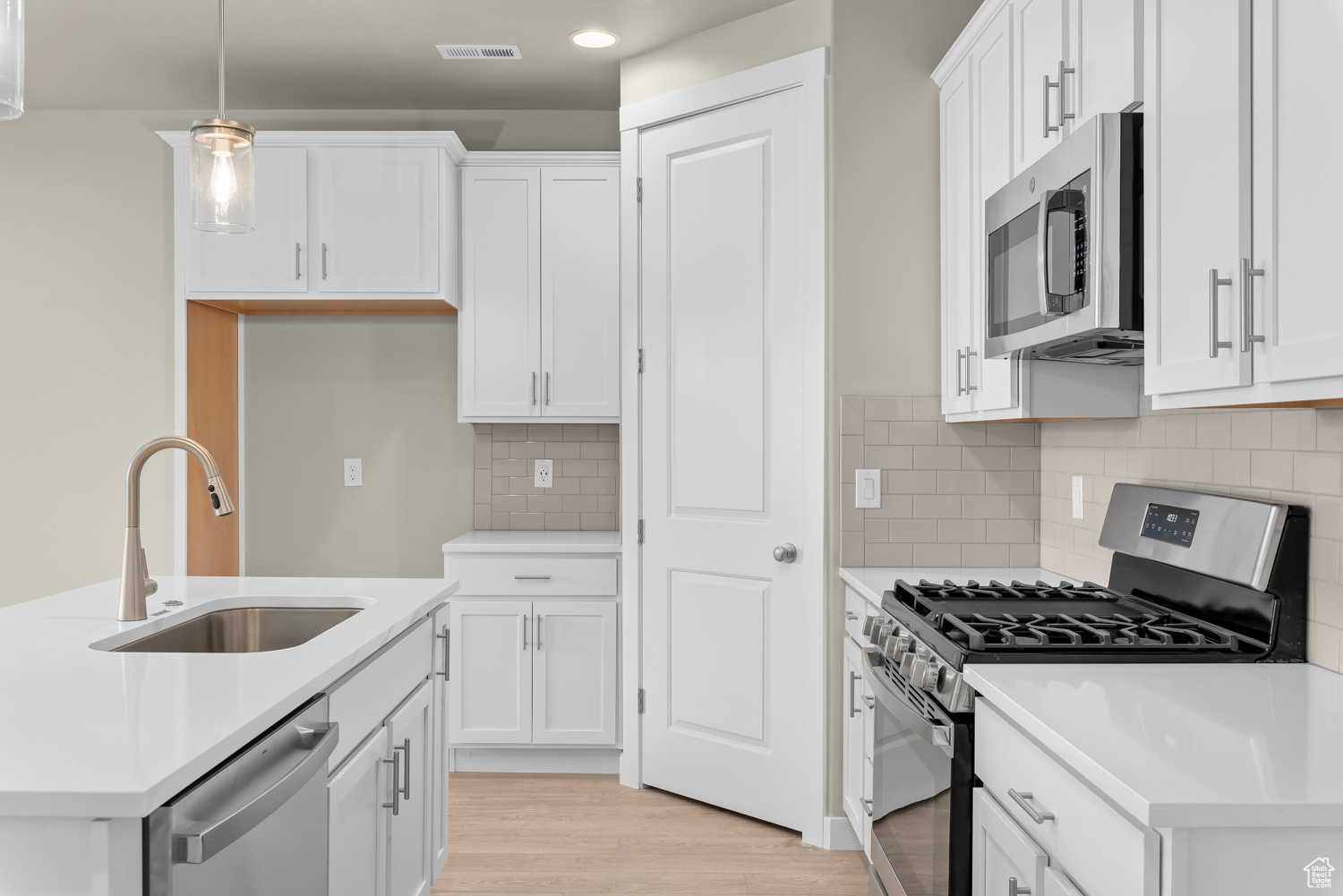 Kitchen with appliances with stainless steel finishes, sink, white cabinets, and pendant lighting