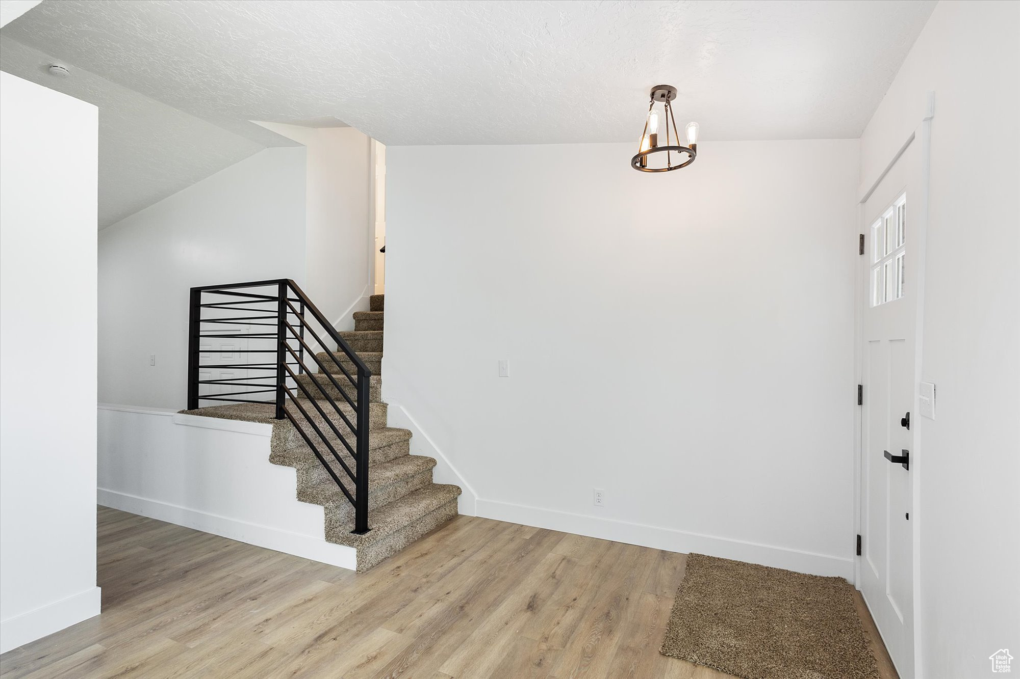 Entryway with light wood-type flooring, an inviting chandelier, a textured ceiling, and vaulted ceiling