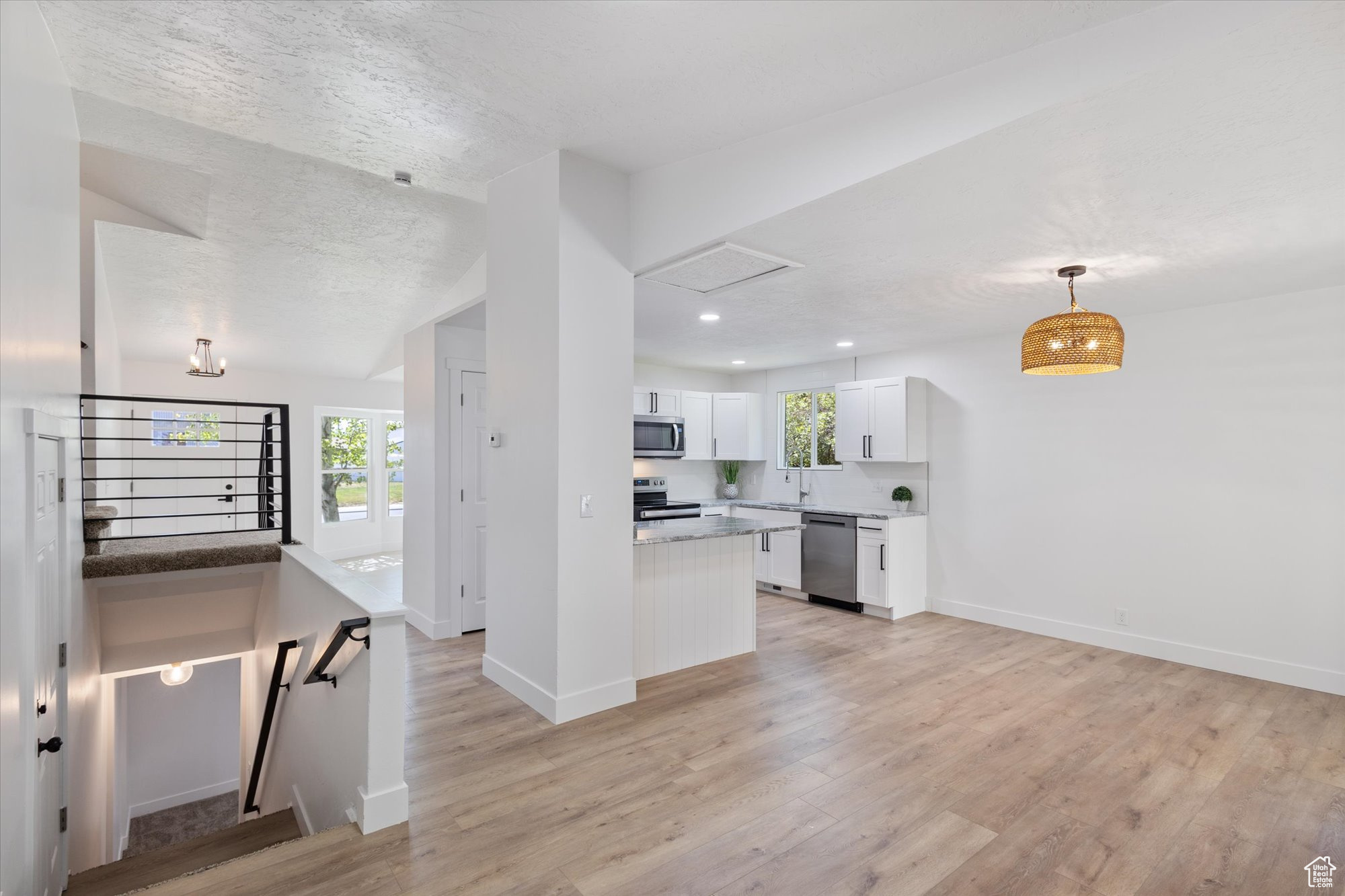 Kitchen featuring light wood-type flooring, a textured ceiling, stainless steel appliances, and white cabinets