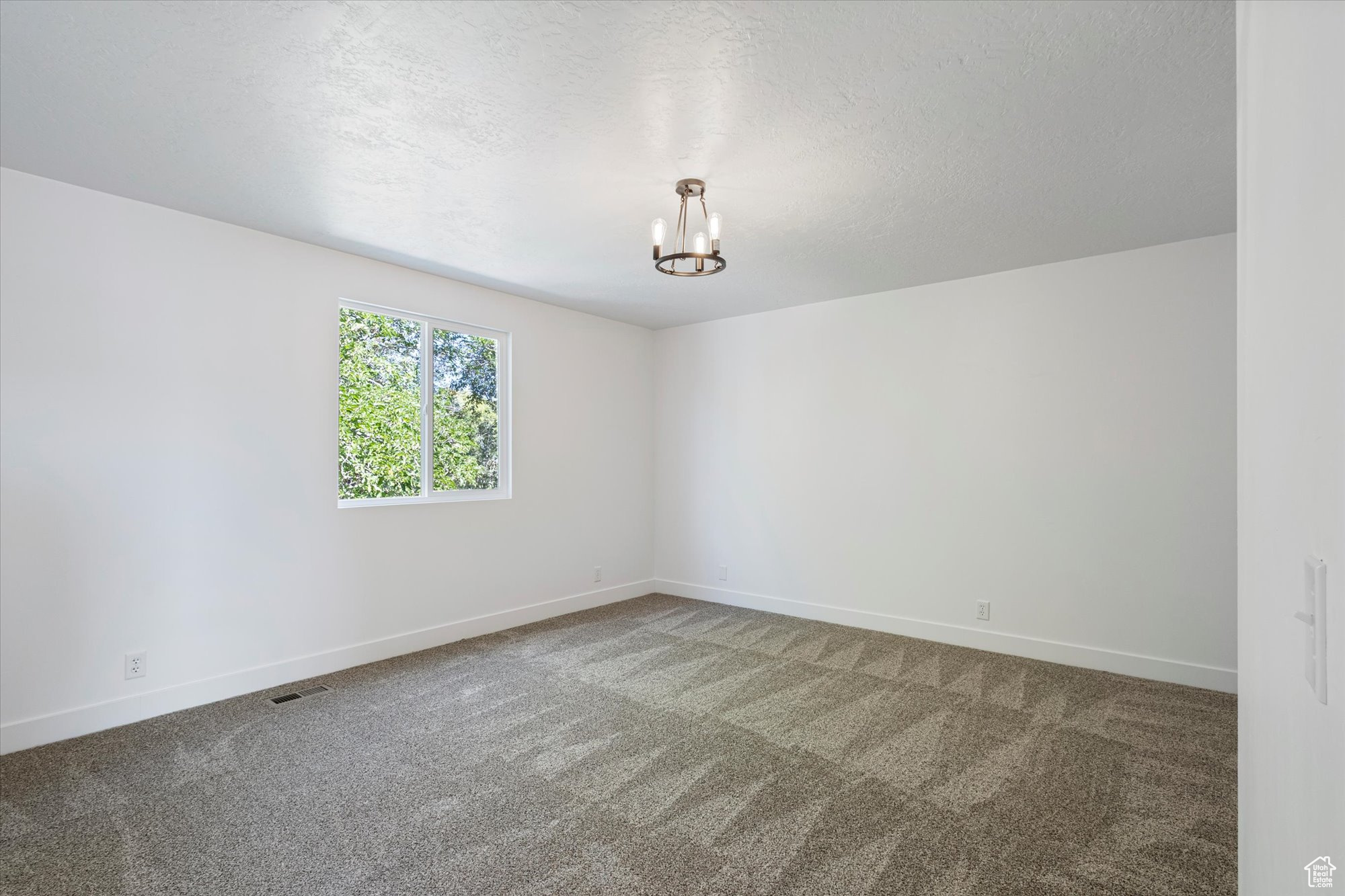 Carpeted spare room featuring a textured ceiling and an inviting chandelier