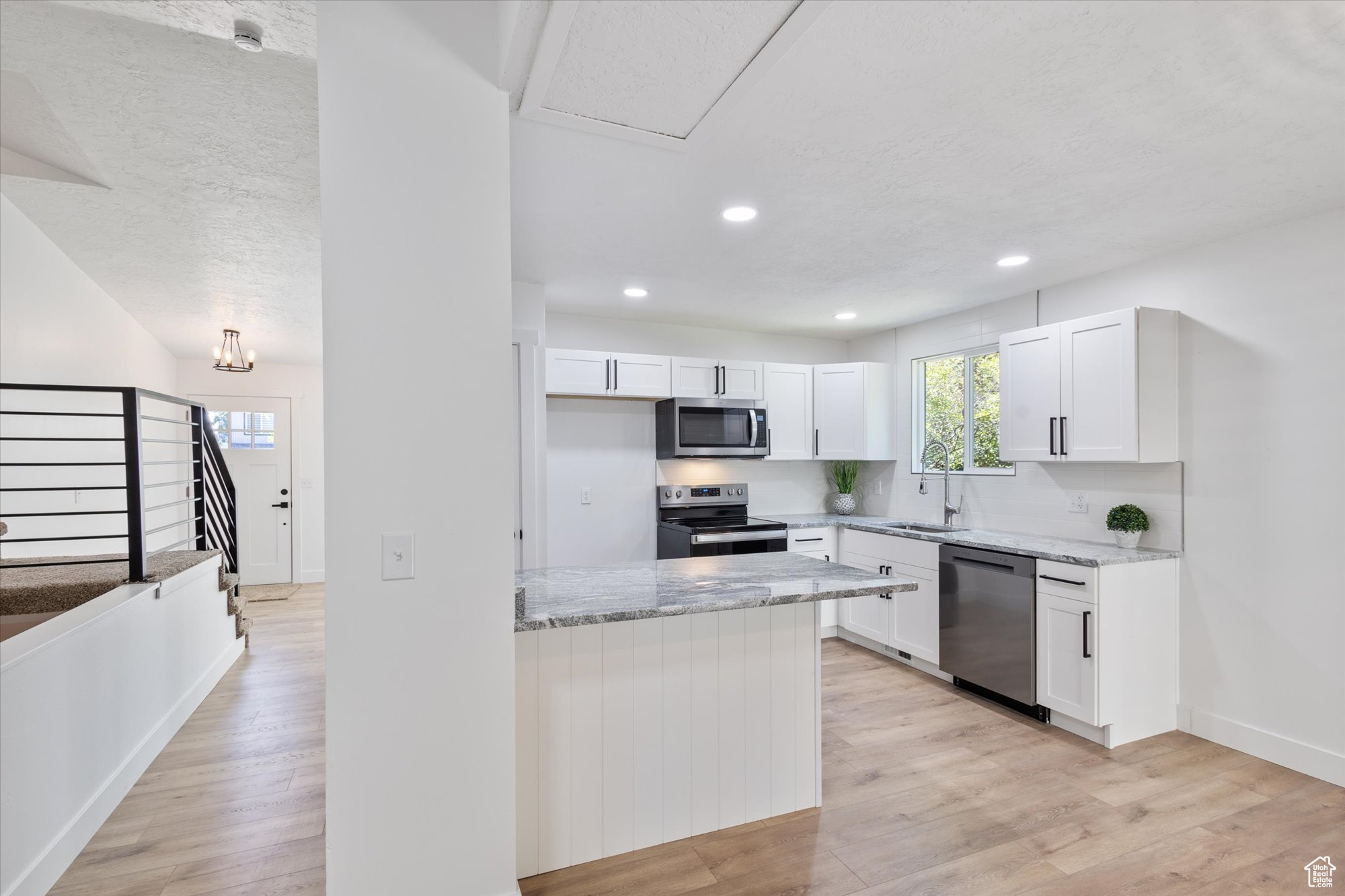 Kitchen featuring light wood-type flooring, light stone counters, appliances with stainless steel finishes, and white cabinetry